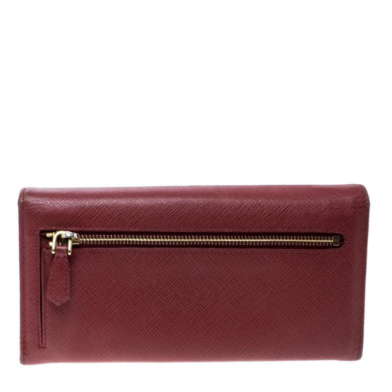 Made of elegant Saffiano leather in bold red, this continental wallet from Prada is a classic. The flap with a snap button opens to a sleek interior featuring multiple card slots and a zipped pocket. This wallet comes with a gold-tone brand