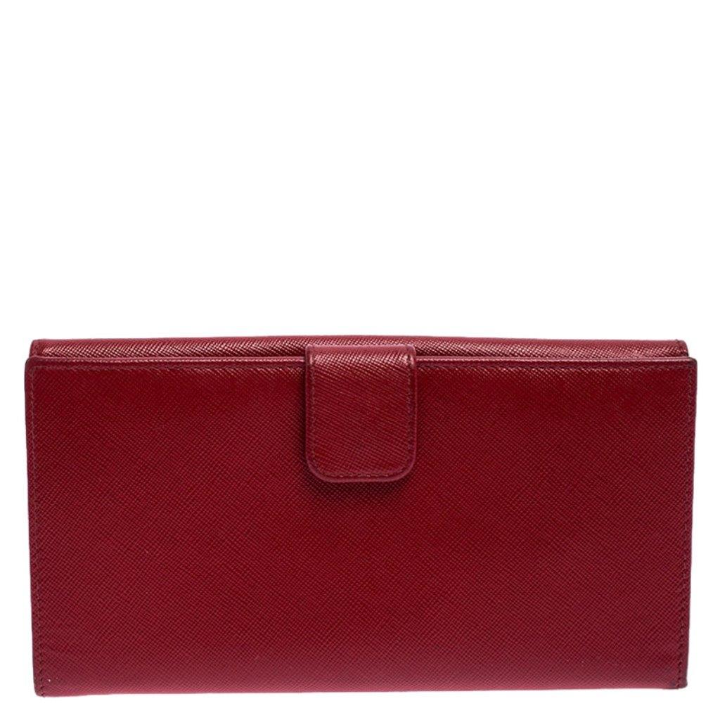 Made of elegant Saffiano Lux leather, this continental wallet from Prada is a classic. The flap with a snap button opens to a sleek interior featuring multiple card slots, open slots and a zipped pocket. This wallet comes with a gold-tone logo on
