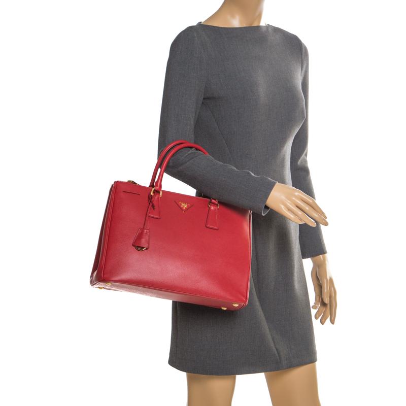 Feminine in shape and grand on design, this double zip tote by Prada will be a loved addition to your closet. It has been crafted from red leather and styled minimally with gold-tone hardware. It comes with two top handles, two zip compartments and