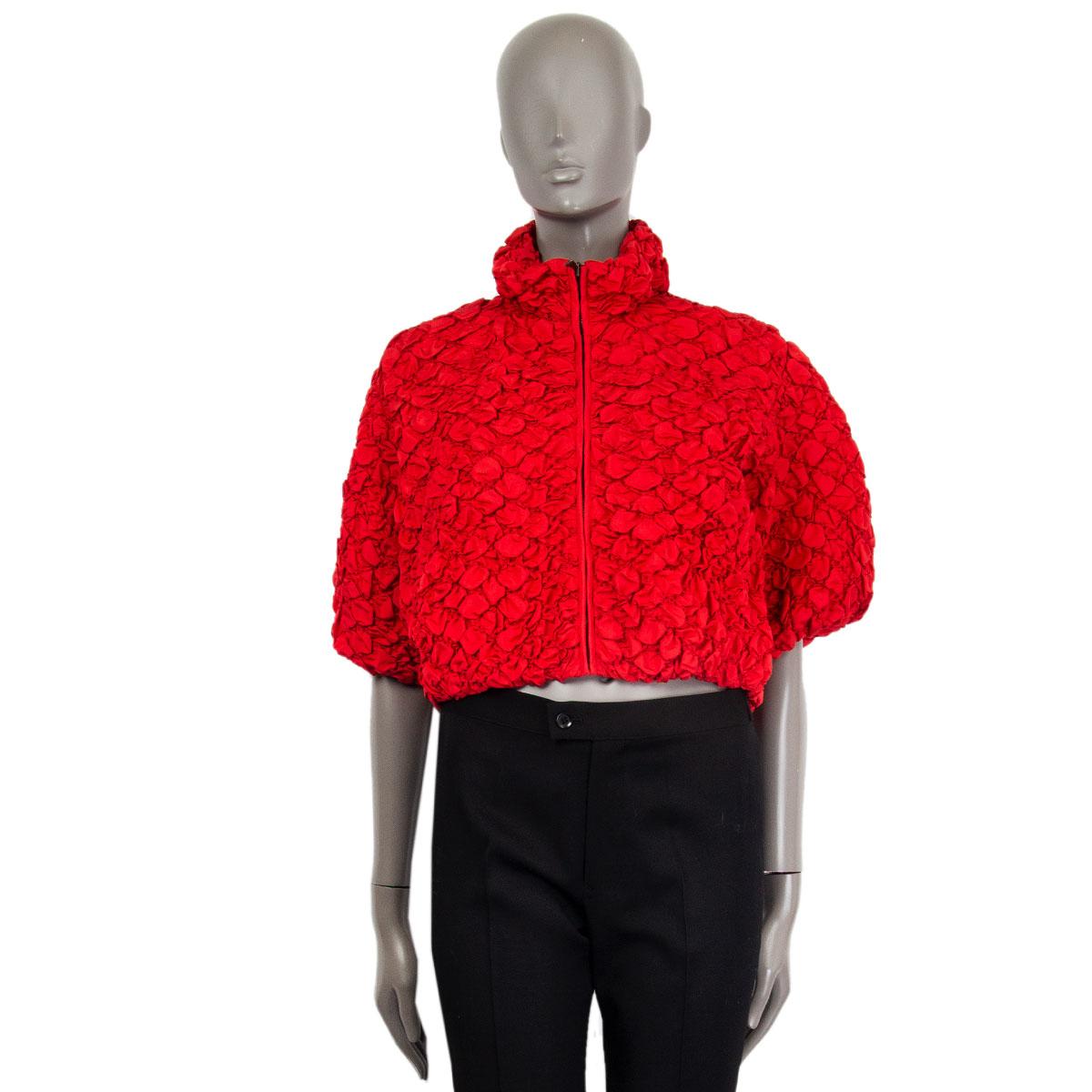 Prada quilted ruched cropped jacket in red silk (56%) and polyester (44%) with a high neck and 3/4 sleeves. Closes on the front with a zipper. Line in silk (assumed as content is missing). Has been worn and is in excellent condition. 

Tag Size 42