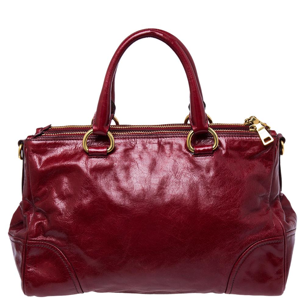This Double Zip tote by Prada is crafted from red leather and gold-toned hardware. It comes with two top handles and two zipped compartments. Additionally, it is provided with protective metal feet and displays the brand logo on the front. This