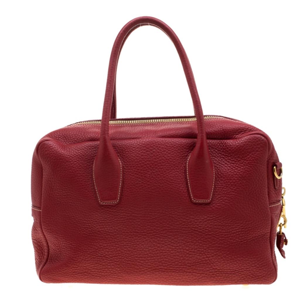 Crafted from Red Vitello Daino leather, this handbag features Prada's iconic logo, top zip closure and gold-tone hardware. This bag is accentuated with dual top handles along with a detachable and adjustable shoulder strap and leather clochette to