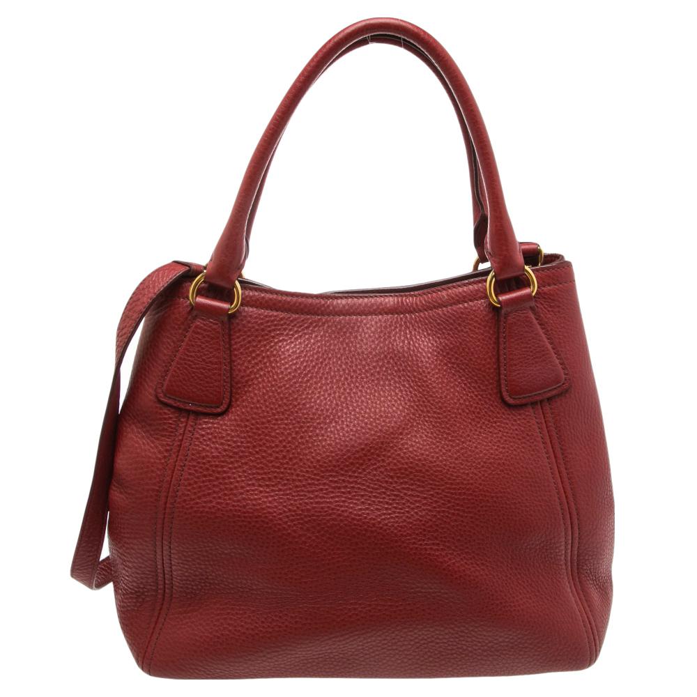 Designed with a classic appeal and functional design, this lovely tote is from the house of Prada. This beauty in red is crafted from Vitello Daino leather and is equipped with two top handles, a shoulder strap, the brand logo at the front, and an