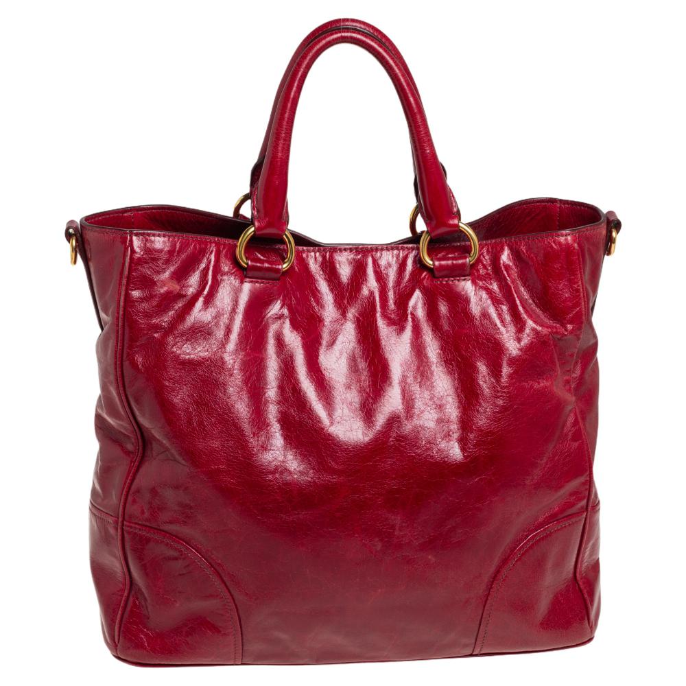 This Tote by Prada makes a timeless handbag you will carry for years to come. Crafted from Vitello Shine leather, the exterior is accented with a Prada label, a leather ID tag, rolled leather handles, a removable shoulder strap, and gold-tone feet.