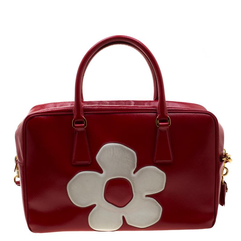 When you carry this Prada creation, be ready to catch admiring glances as this bag is stylish and handy. The bag has been crafted from Saffiano patent leather in a lovely red shade and features a contrasting white floral design on the exterior. It