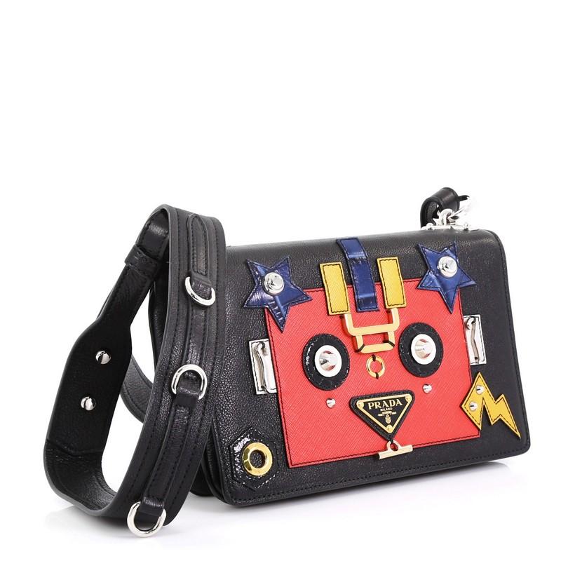 This Prada Robot Flap Shoulder Bag Mixed Media Leather Small, crafted in black leather with robot motif, features a chain-link strap with leather pad, signature triangle logo plate, and silver and gold-tone hardware. Its snap closure opens to a red