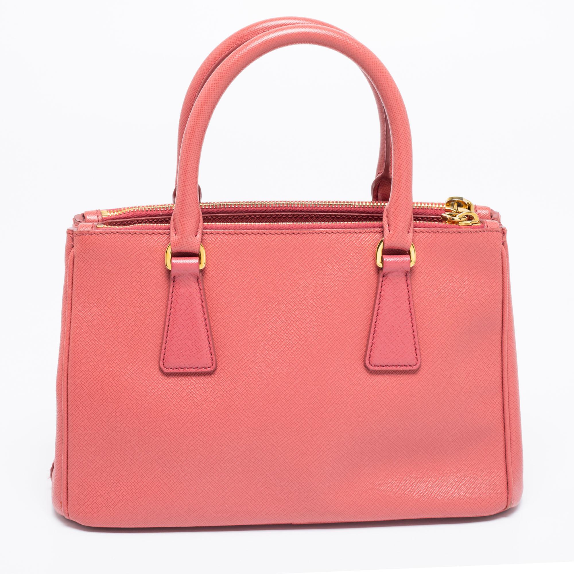 Loved for its classic appeal and functional design, this is one of the most iconic and popular bags from the house of Prada. This beauty in pink is crafted from Saffiano leather and is equipped with two top handles, the brand logo on the front, and