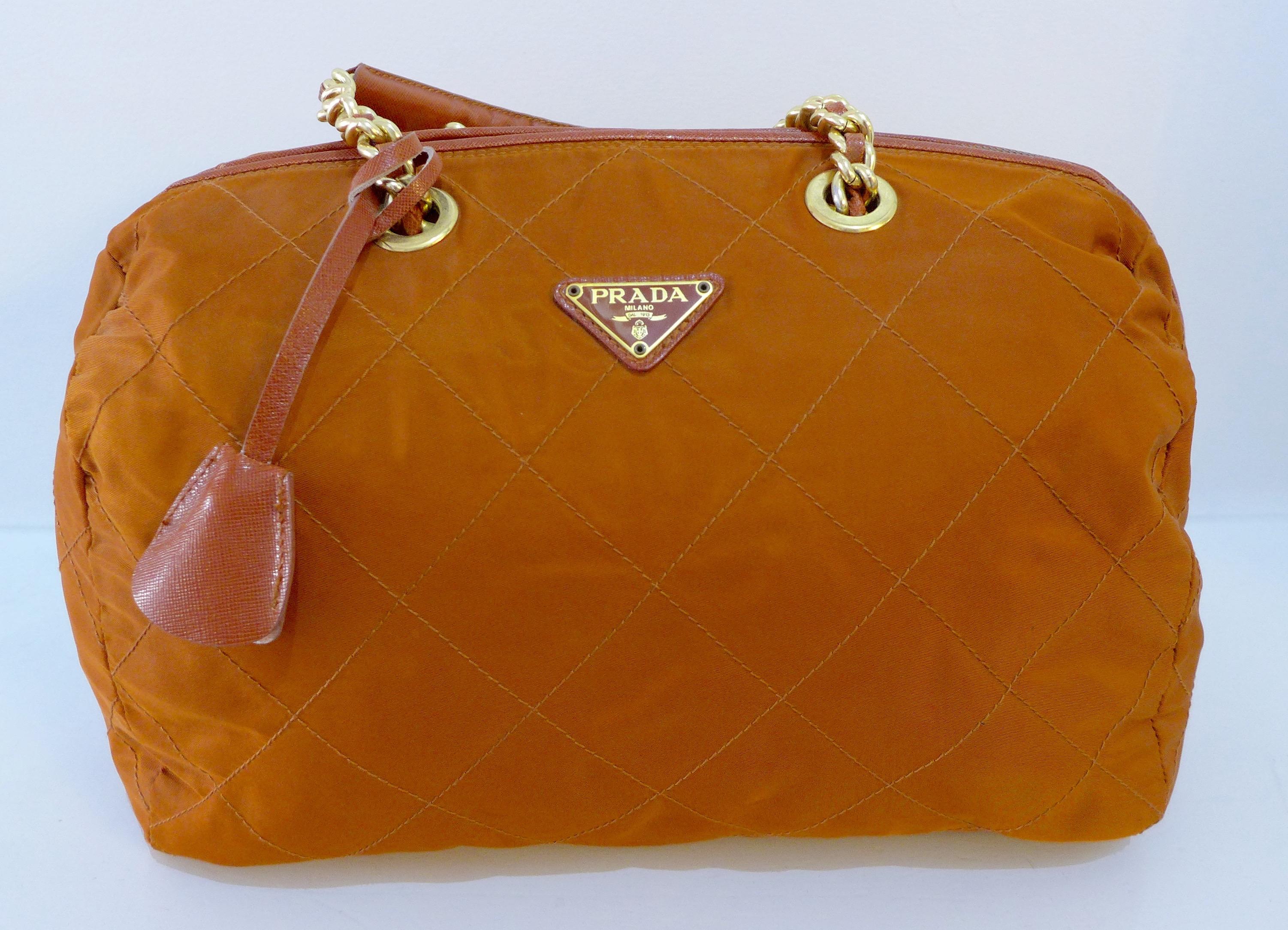 This Prada nylon shoulder bag features a chain and leather strap, rust quilted body, zipper closure, inside pocket, and grey logo interior. 

Measurements in Inches: 
Height: 11
Width: 15
Length: 8
Straps: 17