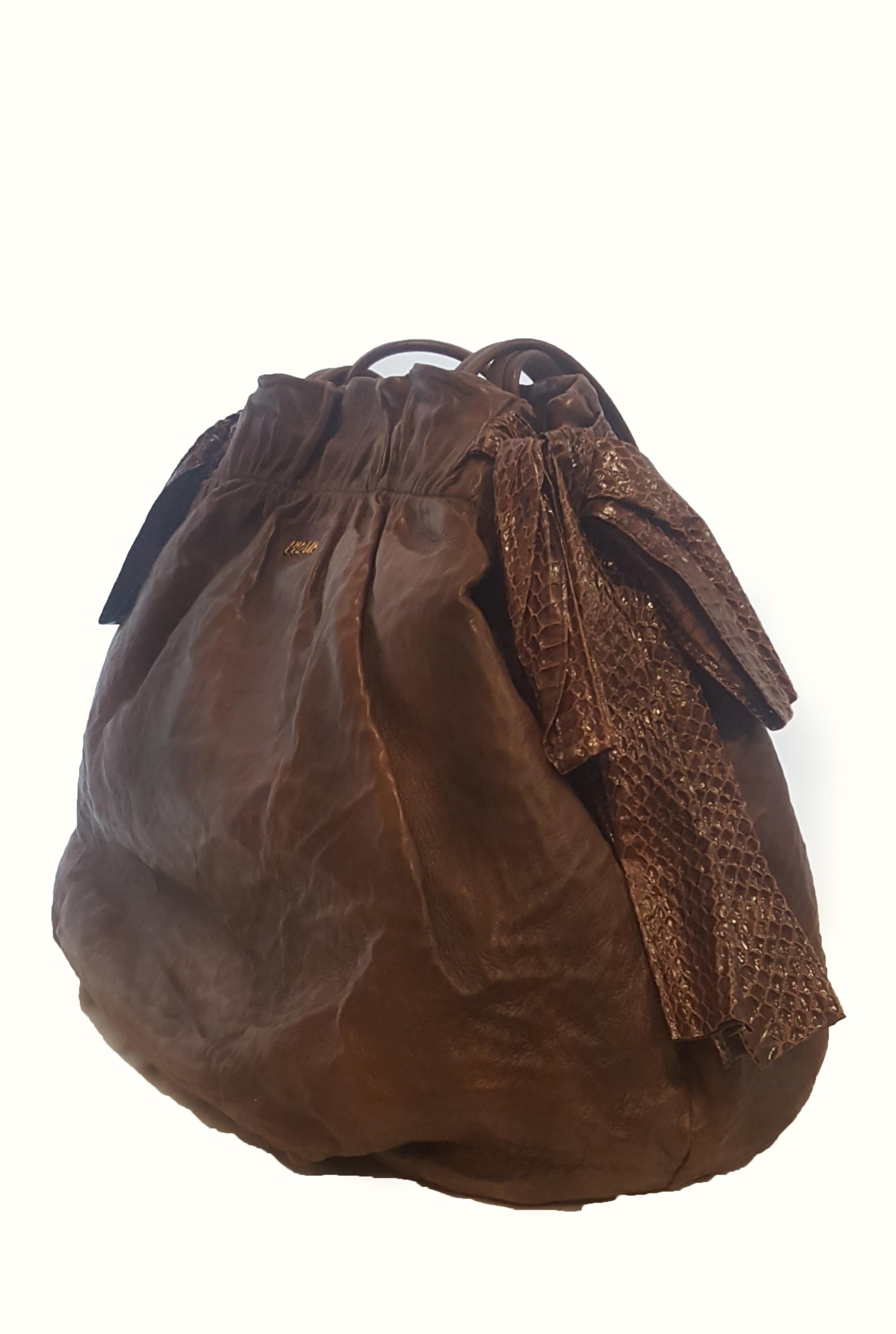 Prada Sabbia Nappa large antique bow satchel in brown, is a beautiful bag with signature details from the Italian brand. The bag features decorative brown snakeskin bows on each side.  Gathered at the top that includes a pressure snap for closure. 