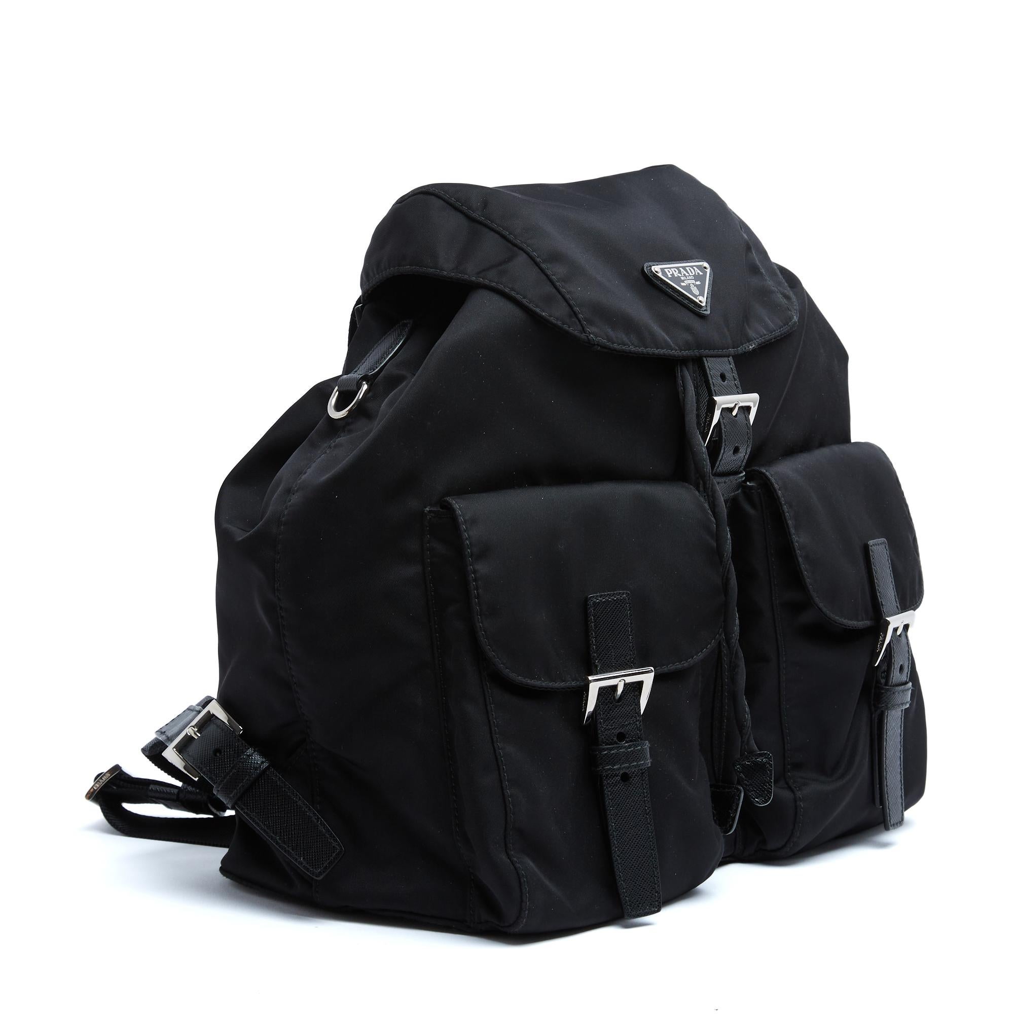 Sac à dos Prada en toile Nylon Re et cuir noir, logo en émail noir sur le rabat fermé par une boucle ardillon, comme les 2 poches avant, bretelles réglables. Largeur 30 cm x hauteur 32 cm x profondeur 15 cm. Le sac est en excellent état, modèle