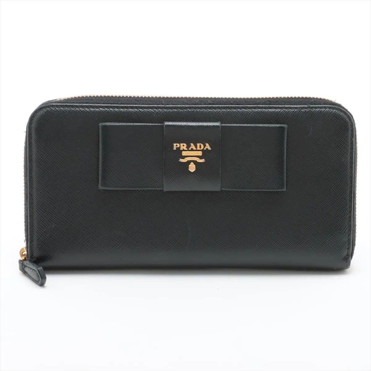 The Prada Saffiano Fiocco Leather Zippy Wallet in black is a timeless and feminine accessory, crafted from the brand’s signature Saffiano leather known for its durability and subtle crosshatch texture. Its sleek silhouette is accented with the