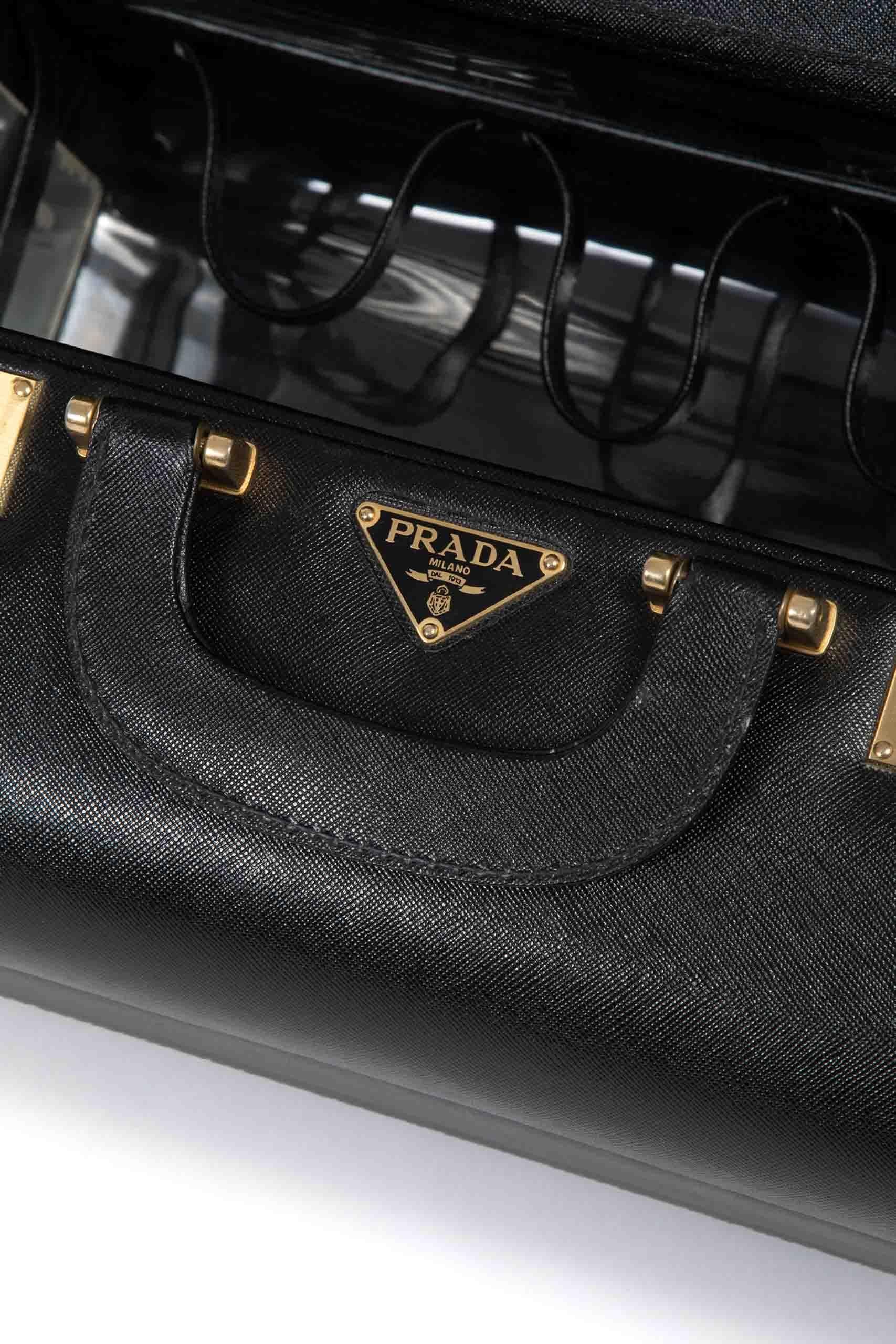 Bel étui Prada fabriqué à la fin des années 1980. Il est réalisé en cuir noir Saffiano, marque de fabrique des bagages et de la maroquinerie Prada. Le beautycase est doté d'une double poignée en cuir, d'une serrure à combinaison numérique, de