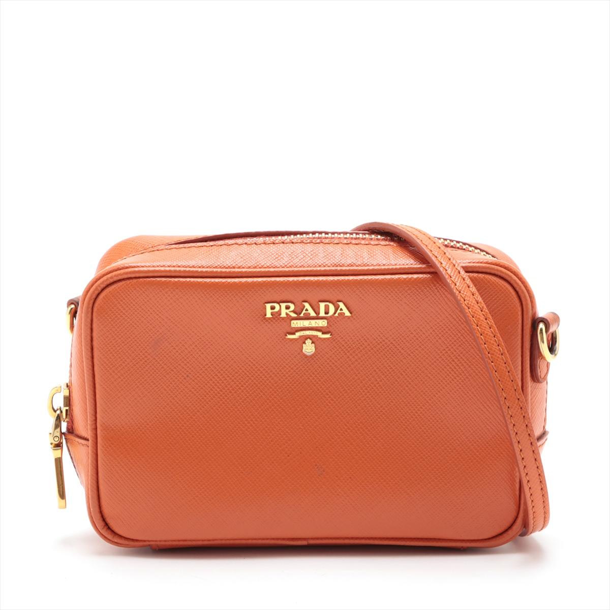 The Prada Saffiano Leather Camera Bag in Orange is a vibrant and stylish accessory that reflects Prada's renowned craftsmanship and contemporary design aesthetic. The camera bag features the iconic Saffiano leather, known for its distinctive