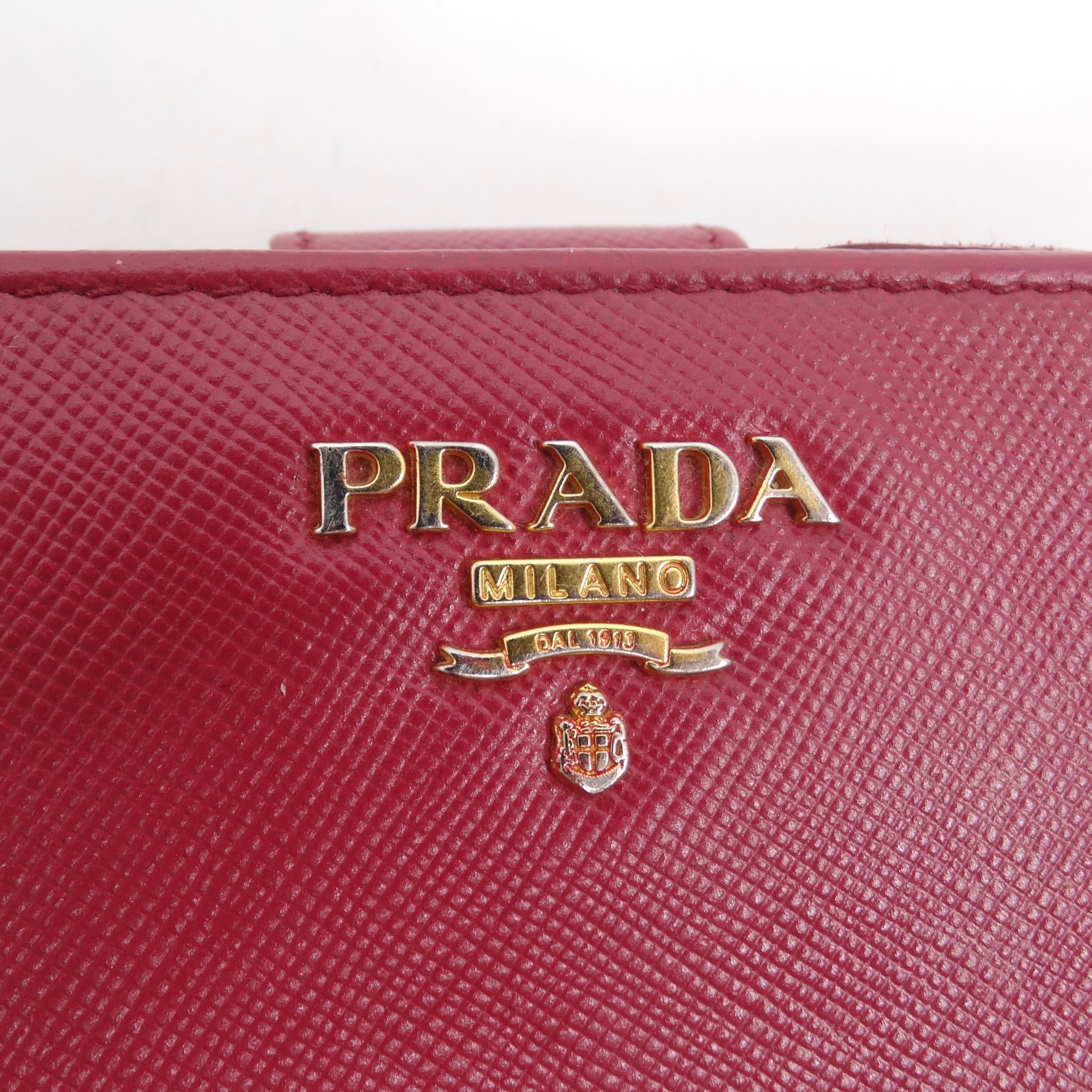 Laissez-vous séduire par l'élégance du portefeuille compact en cuir Prada en rose, un accessoire chic qui allie sans effort style et praticité. Confectionné dans le cuir croisé Saffiano, signature de Prada, ce portefeuille n'est pas seulement un