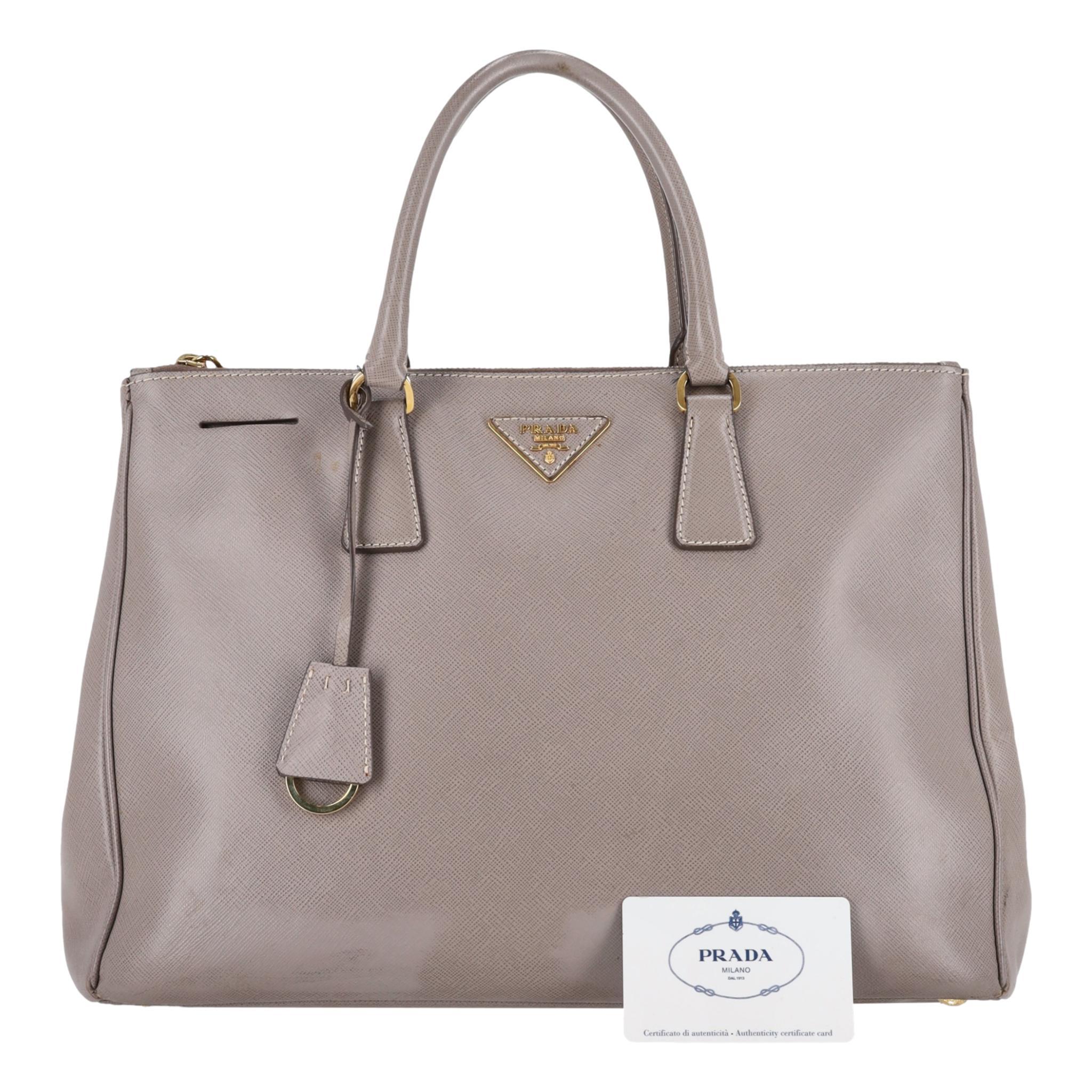 Bolso Tote Prada de piel saffiano con doble cremallera Galleria

Bolso tote gris confeccionado en piel saffiano de grano grueso.

Lleva el logotipo triangular de Prada en el centro, herrajes dorados y cierre de cuero.

Con asas superiores