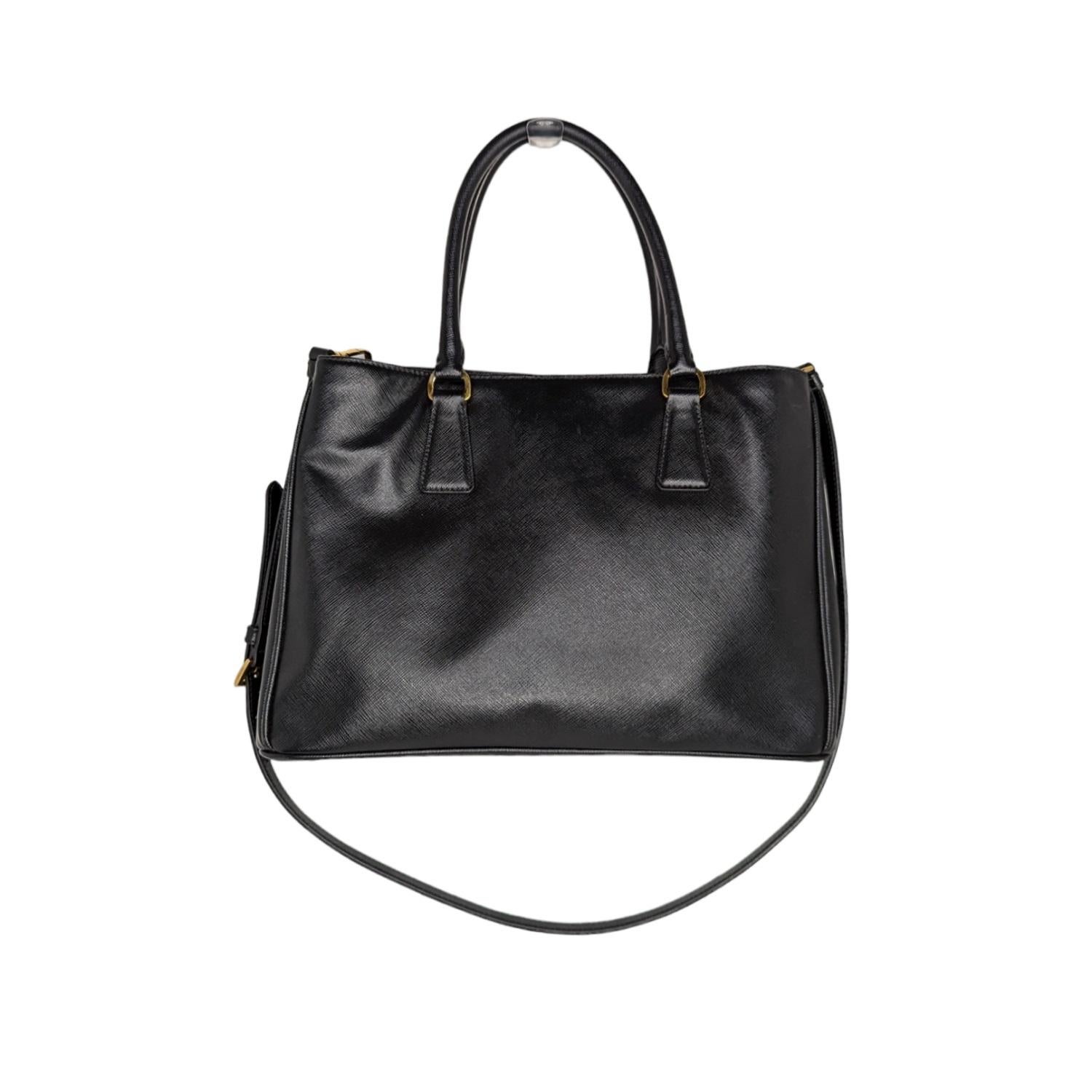 This chic tote is crafted of black saffiano cross-grain leather. The tote features rolled leather top handles, an optional shoulder strap, a hanging key clochette, and polished brass hardware including a Prada triangle logo on the front. The top is