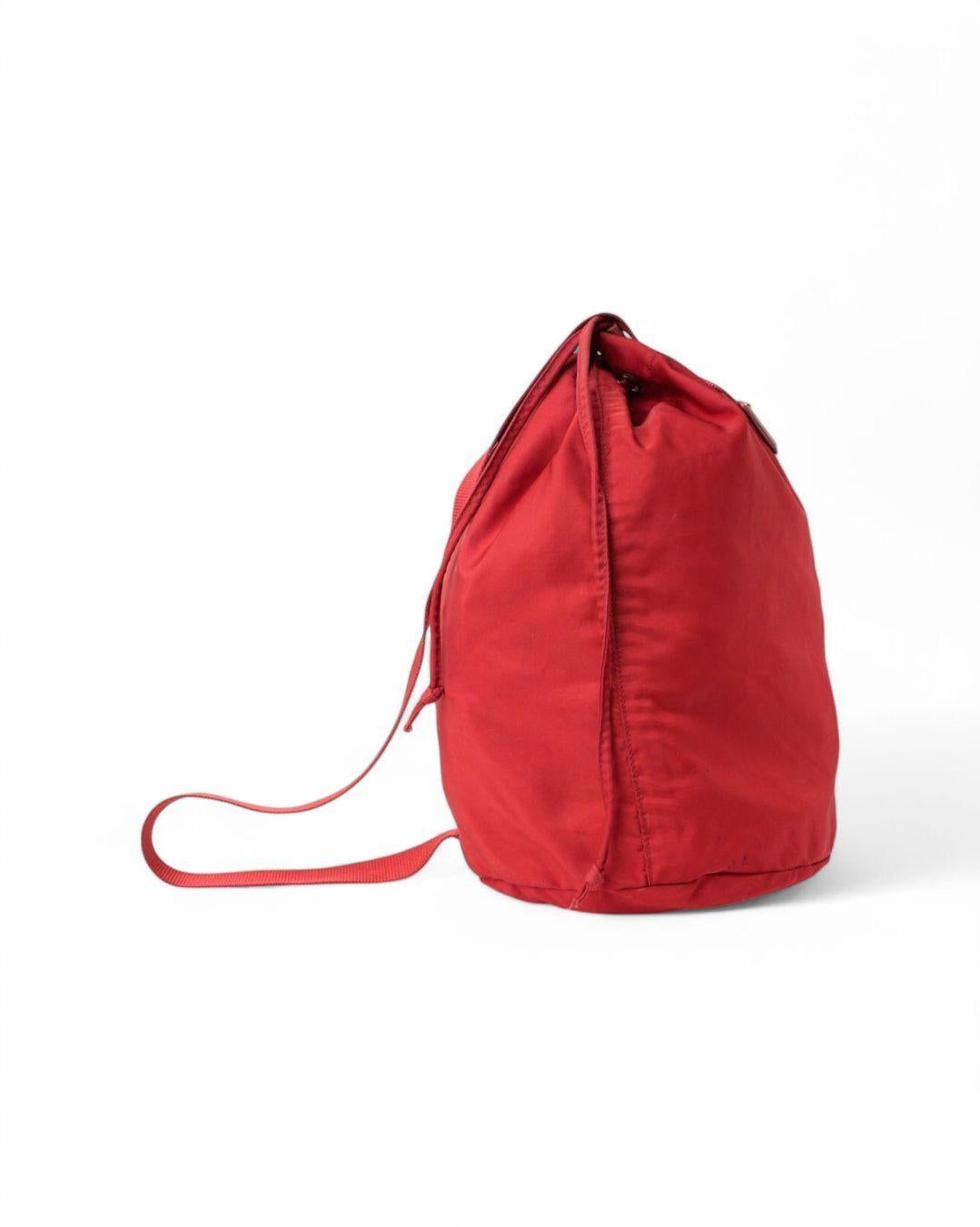 Prada signature bucket, in size MM,  made of red nylon with silver hardware. Equipped with a drawstring top closure, internally lined with tone-on-tone Nylon, quite roomy. Equipped with a fabric handle for shoulder or hand carrying. The item is in