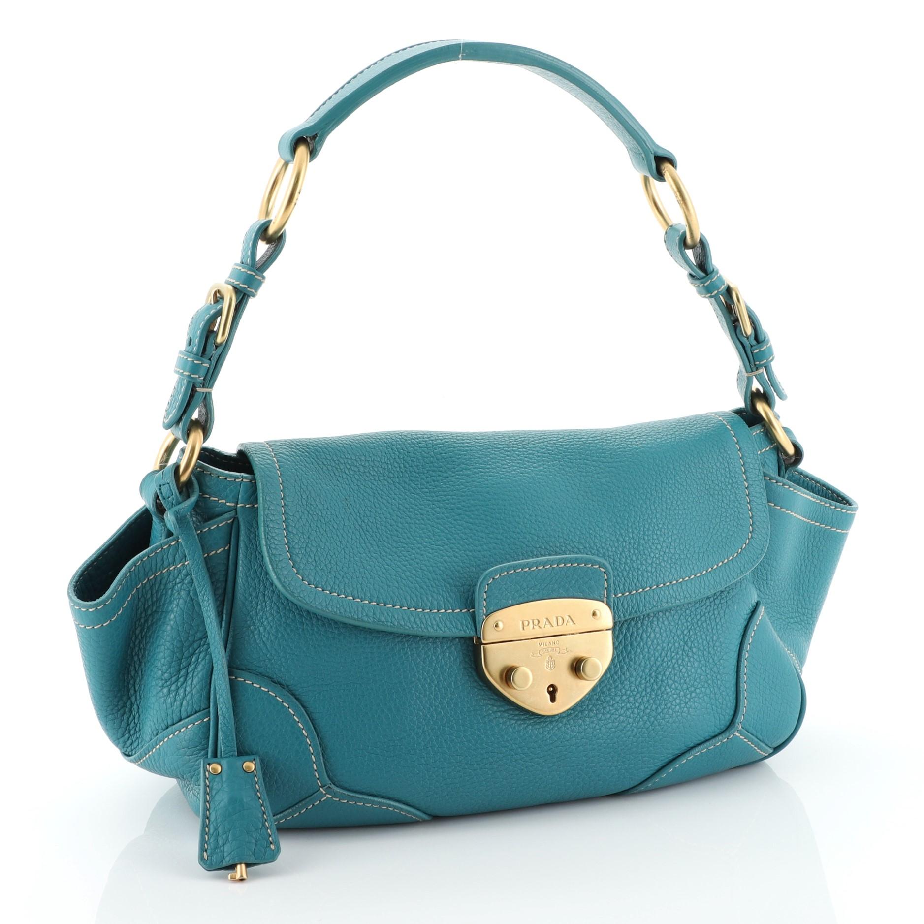 This Prada Side Pocket Flap Shoulder Bag Vitello Daino Medium, crafted from blue vitello daino leather, features flat leather shoulder strap with buckle details, raised Prada logo lettering at front, dual flap pockets at sides and matte gold-tone