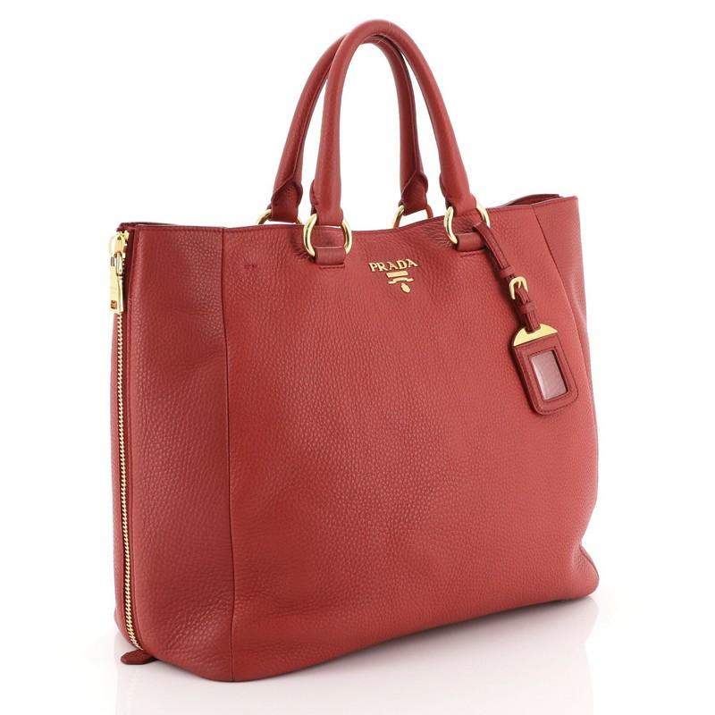 This Prada Side Zip Convertible Shopper Tote Vitello Daino Large, crafted from red vitello daino leather, features dual rolled handles, raised Prada logo at its center, and gold-tone hardware. Its snap closure opens to a red fabric interior with