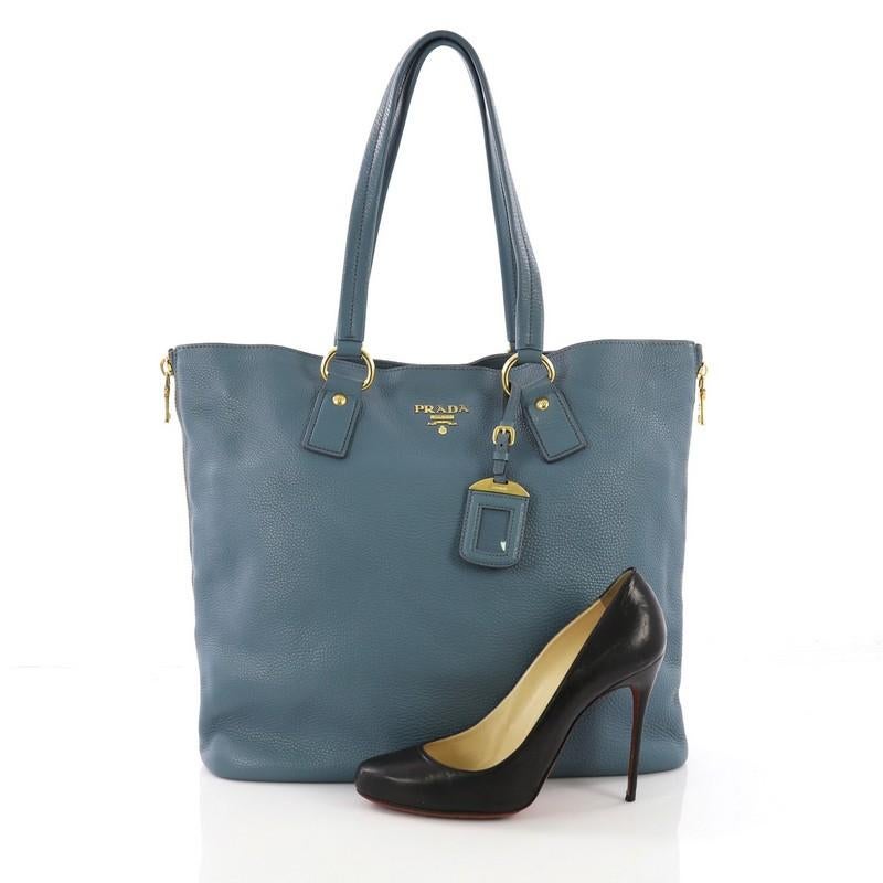 This Prada Side Zip Shopper Tote Vitello Daino Large, crafted from blue vitello daino leather, features dual tall flat leather handles, zippered side gussets, and gold-tone hardware. Its magnetic snap closure opens to a blue fabric interior with