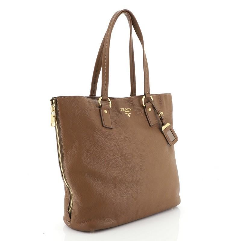 This Prada Side Zip Shopper Tote Vitello Daino Large, crafted from brown vitello daino leather, features dual tall flat leather handles, zippered side gussets, and gold-tone hardware. Its magnetic snap closure opens to a brownk fabric interior with