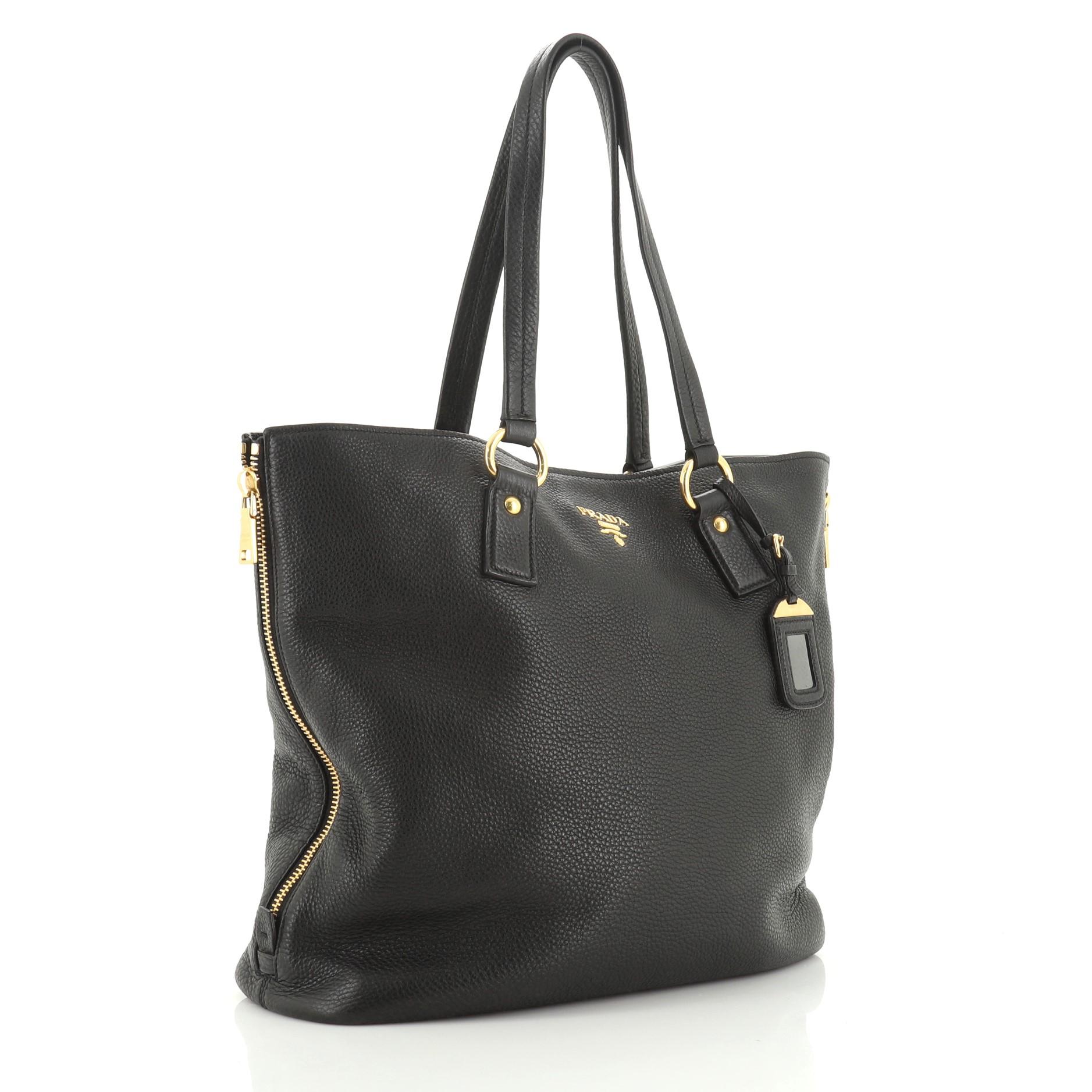 This Prada Side Zip Shopper Tote Vitello Daino Large, crafted from black vitello daino leather, features dual tall flat leather handles, zippered side gussets, and gold-tone hardware. Its snap closure opens to a black fabric interior with side zip