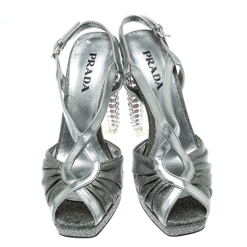 Silvery incandescence greets us with the shimmering fabric and leather exterior of these gorgeous Prada sandals! They feature a peep-toe silhouette and cutout-detailed vamp straps. They come equipped with buckled slingbacks, comfortable insoles and