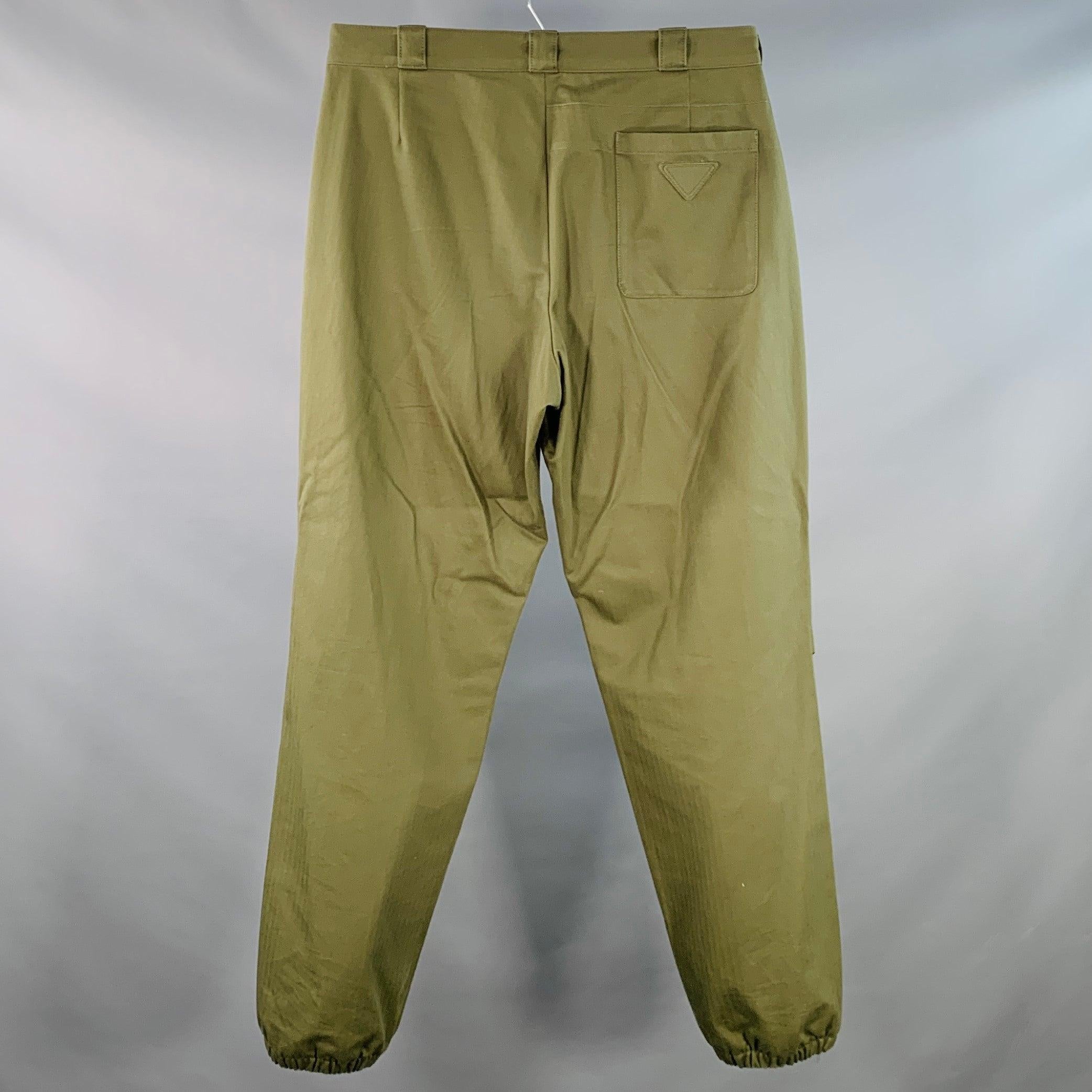Pantalon décontracté PRADA en coton tissé vert olive avec motif à chevrons, jambe fuselée avec poignets élastiques et fermeture à glissière. Fabriqué en Italie. Très bon état. Marques et signes d'usure mineurs. 

Marqué :   IT 52 

Mesures : 
 