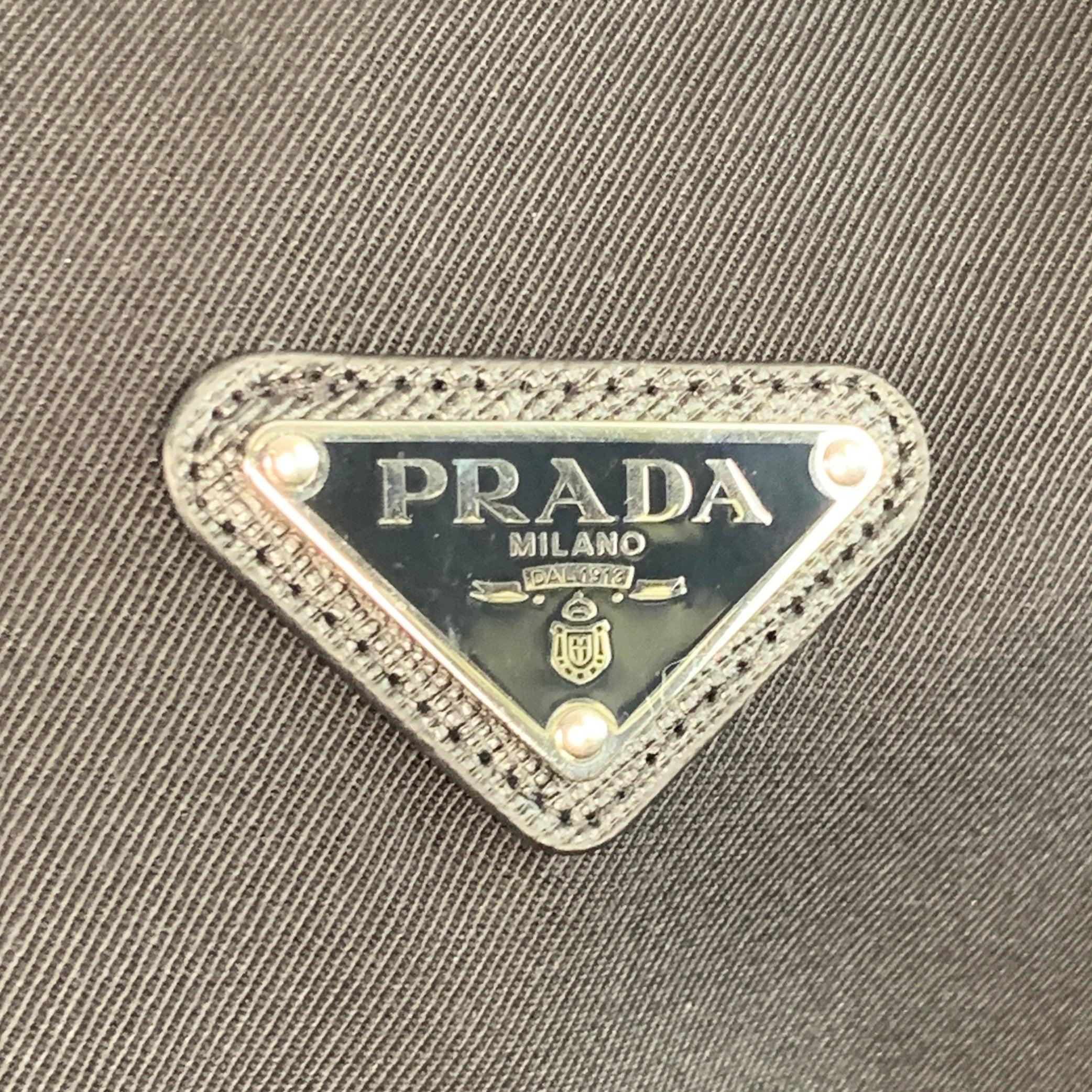 Giacca camicia di Prada in twill di lana vergine nera sfoderata con colletto in raso nero tono su tono e dettagli a righe laterali in raso, una tasca interna in raso, logo a triangolo in metallo argentato e chiusura con zip. Made in Italy.