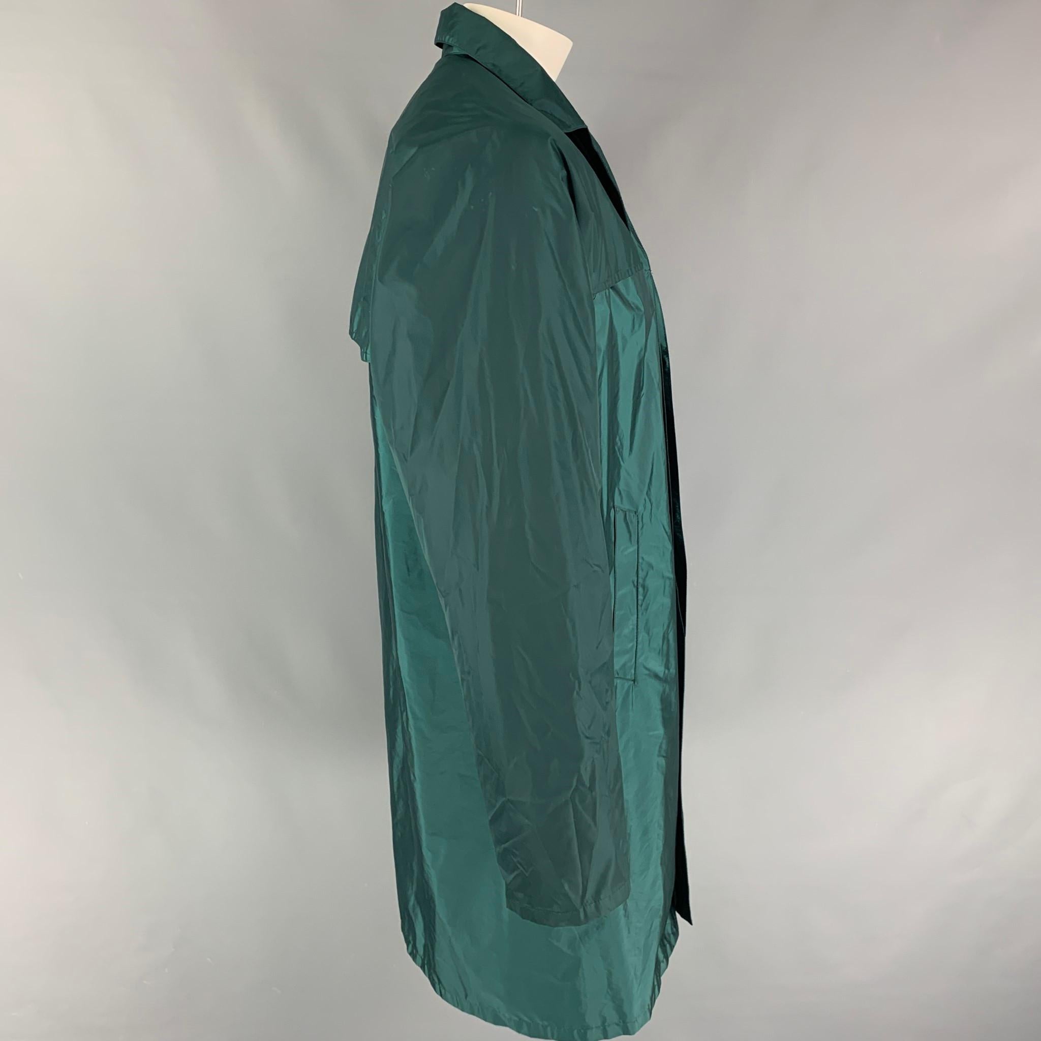 PRADA trench coat comes in a green nylon blend featuring a spread collar, slit pockets, and a hidden placket closure. Made in Italy. 

Very Good Pre-Owned Condition.
Marked: XL

Measurements:

Shoulder: 17 in.
Chest: 48 in.
Sleeve: 27 in.
Length: