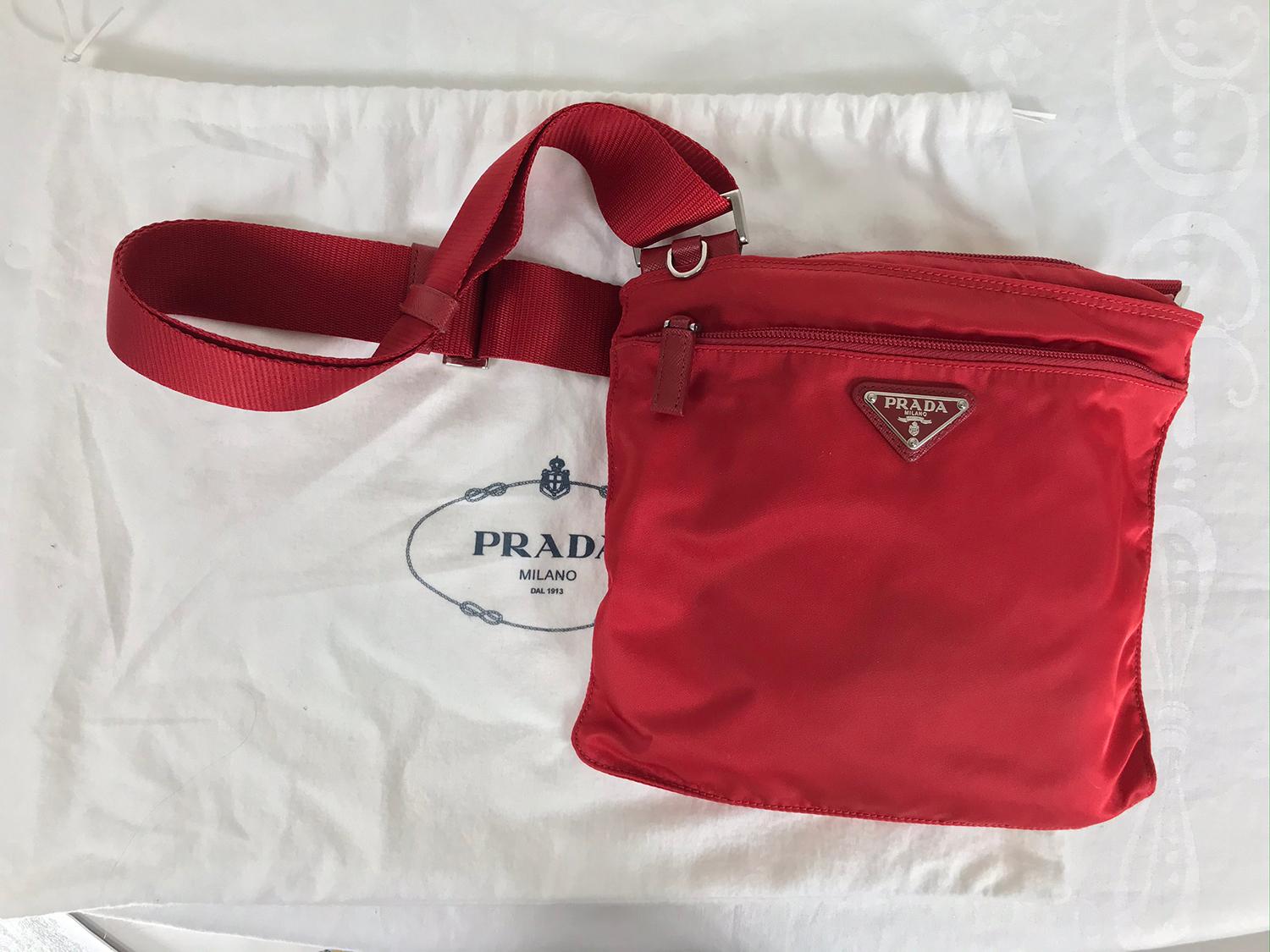 Prada small nylon cross body handbag in red. This bag looks barely, if ever, used, with the protector bag. Nylon pouch with outside zipper compartment, leather zipper pull tab. Prada silver triangle logo at the front, Prada metal tag inside in red
