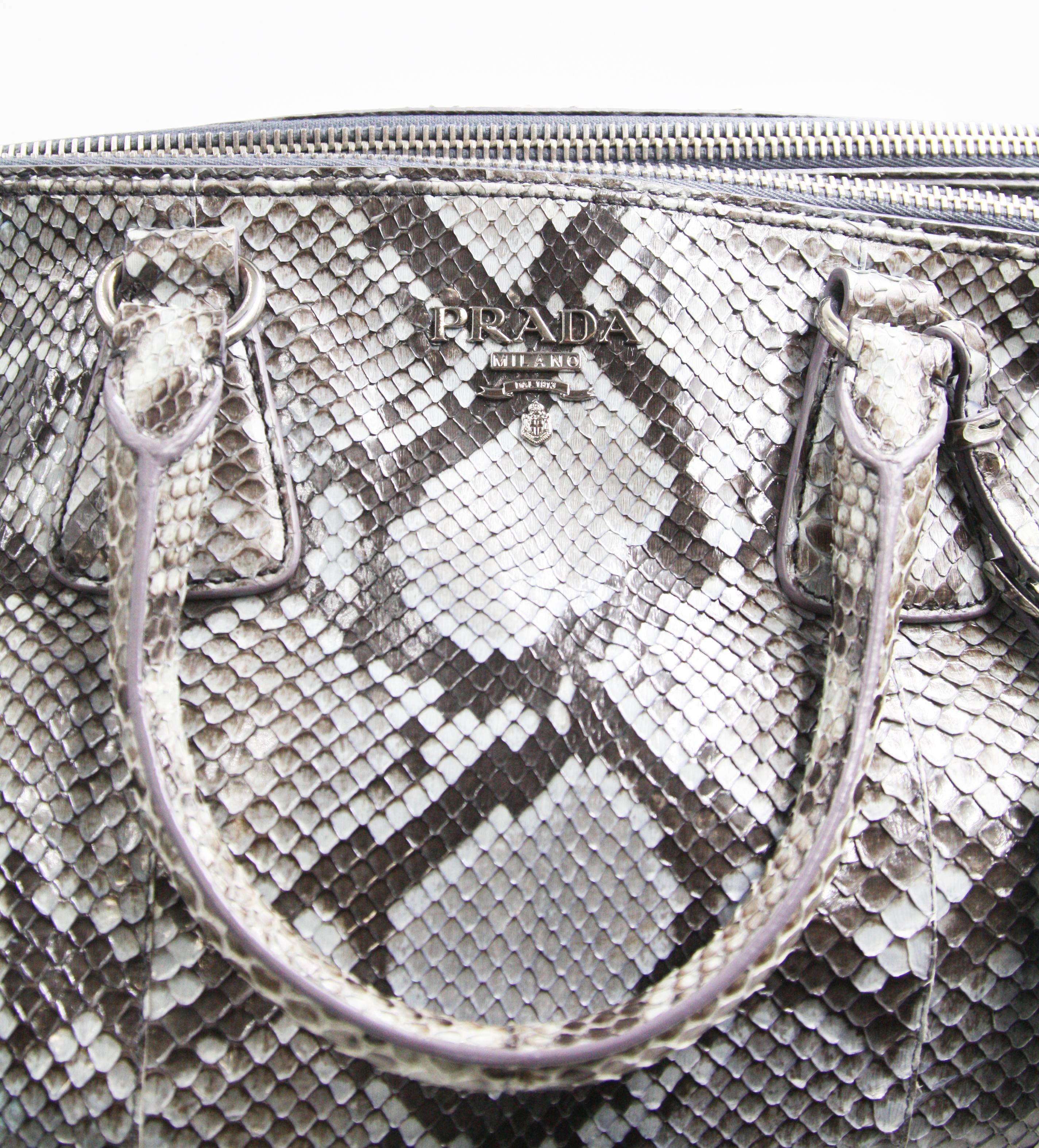 his Prada Tote Python Large, crafted from genuine gray python, features dual rolled handles, raised Prada logo, and silver-tone hardware. It opens to a pale pink leather interior with two zip compartments on both sides and an open top middle
