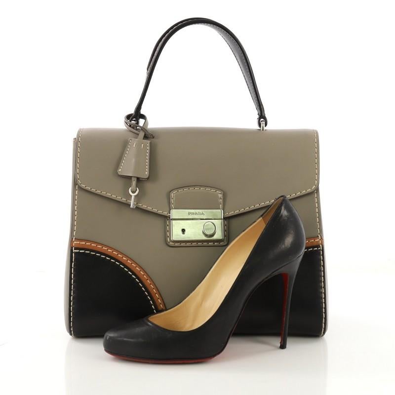 This Prada Sound Top Handle Bag Calfskin Medium, crafted in gray calfskin leather, features a short top handle, frontal flap with, and silver-tone hardware. Its press-lock closure opens to a gray leather interior with zip pocket. **Note: Shoe