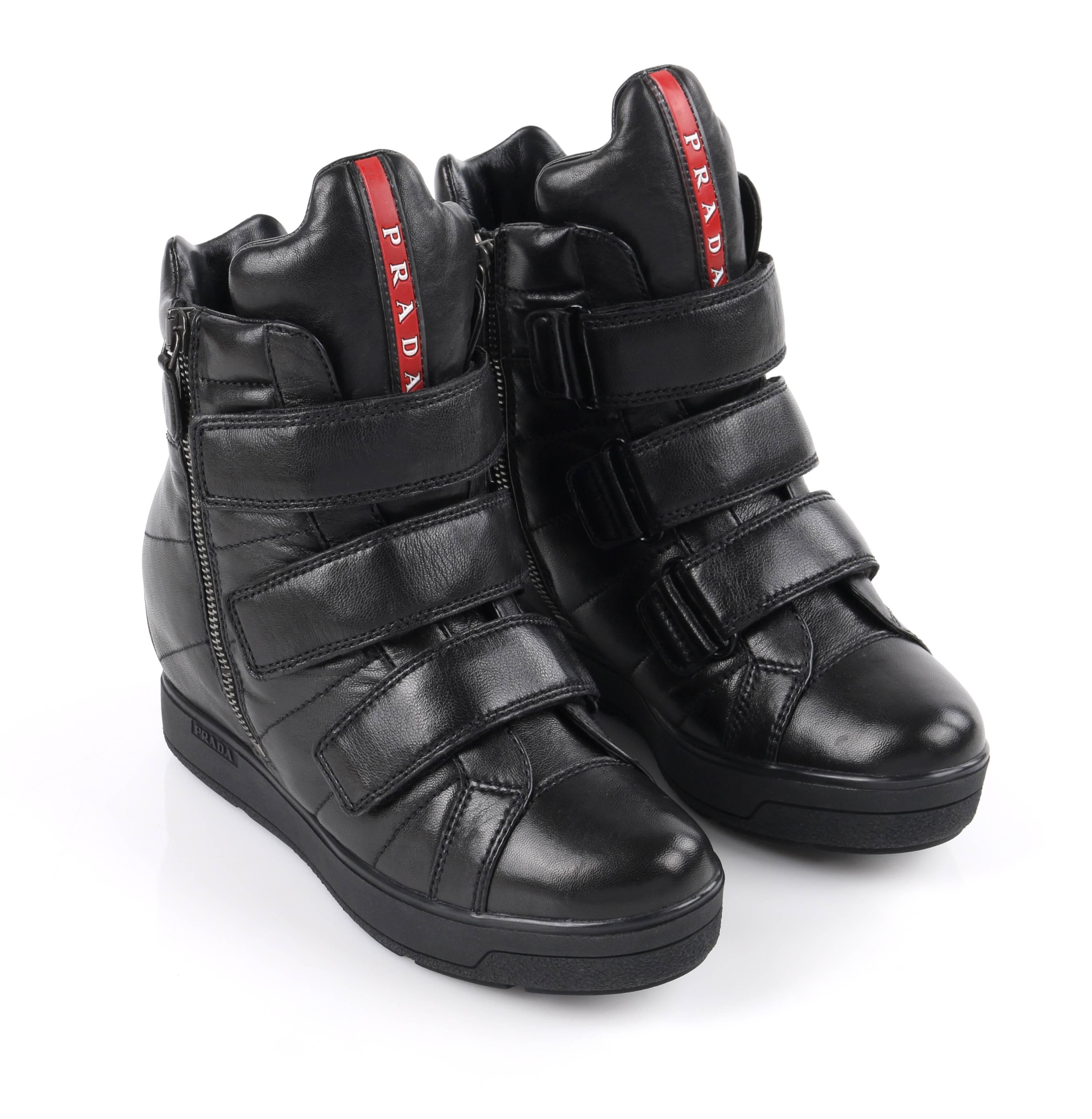 Prada Sport Autumn / Winter 2013 black vitello leather triple strap hi top wedge sneakers. Designed by Miuccia Prada. Black smooth vitello leather upper. Three adjustable hook and loop straps across front. Two gun-metal toned side seam zippers with