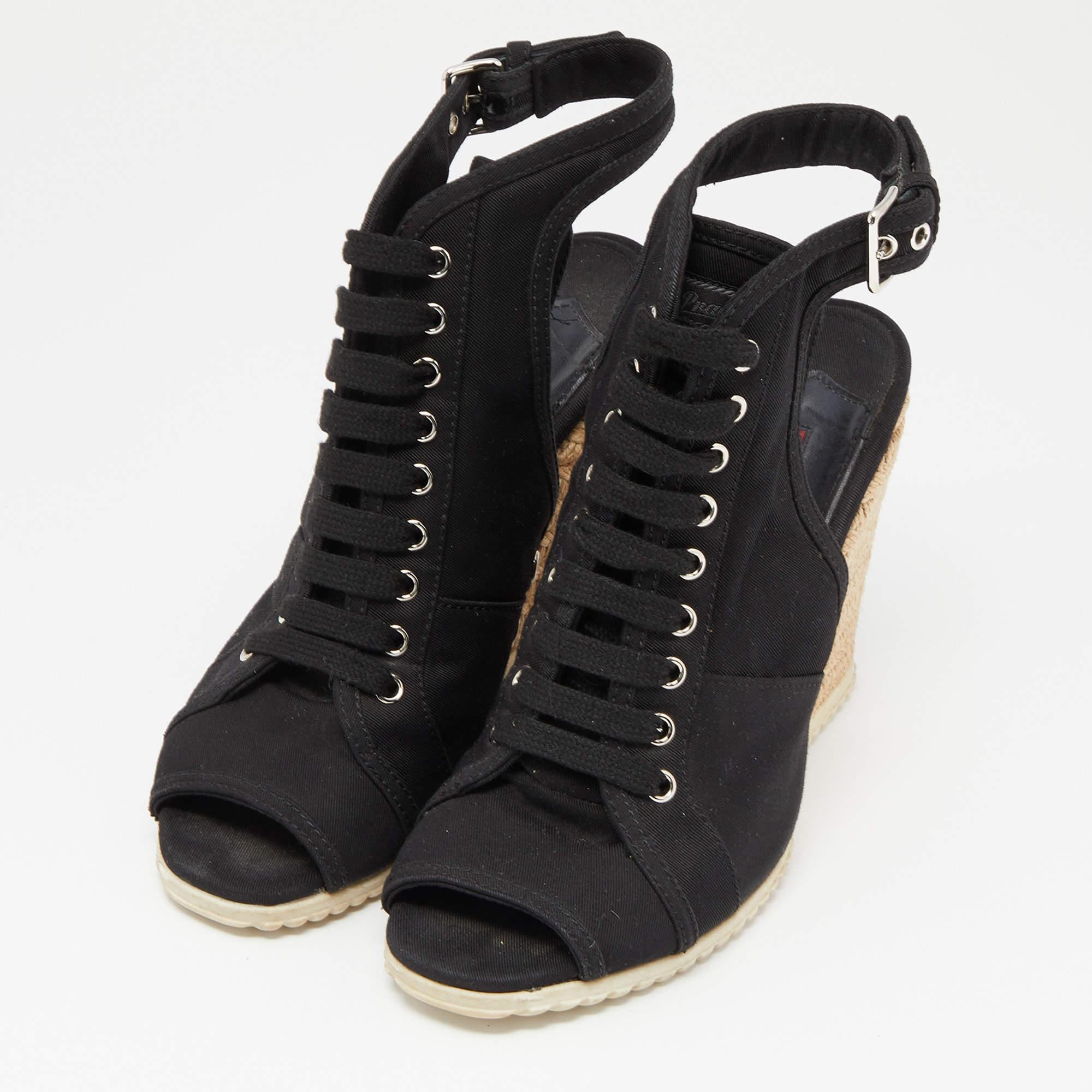 Este par de sandalias de cuña de Prada es ideal para la temporada. Confeccionadas en lona negra, estas alpargatas tienen la pala entrecruzada de piel trenzada y un cierre con correa en el tobillo. Vienen con plantillas forradas de piel para un