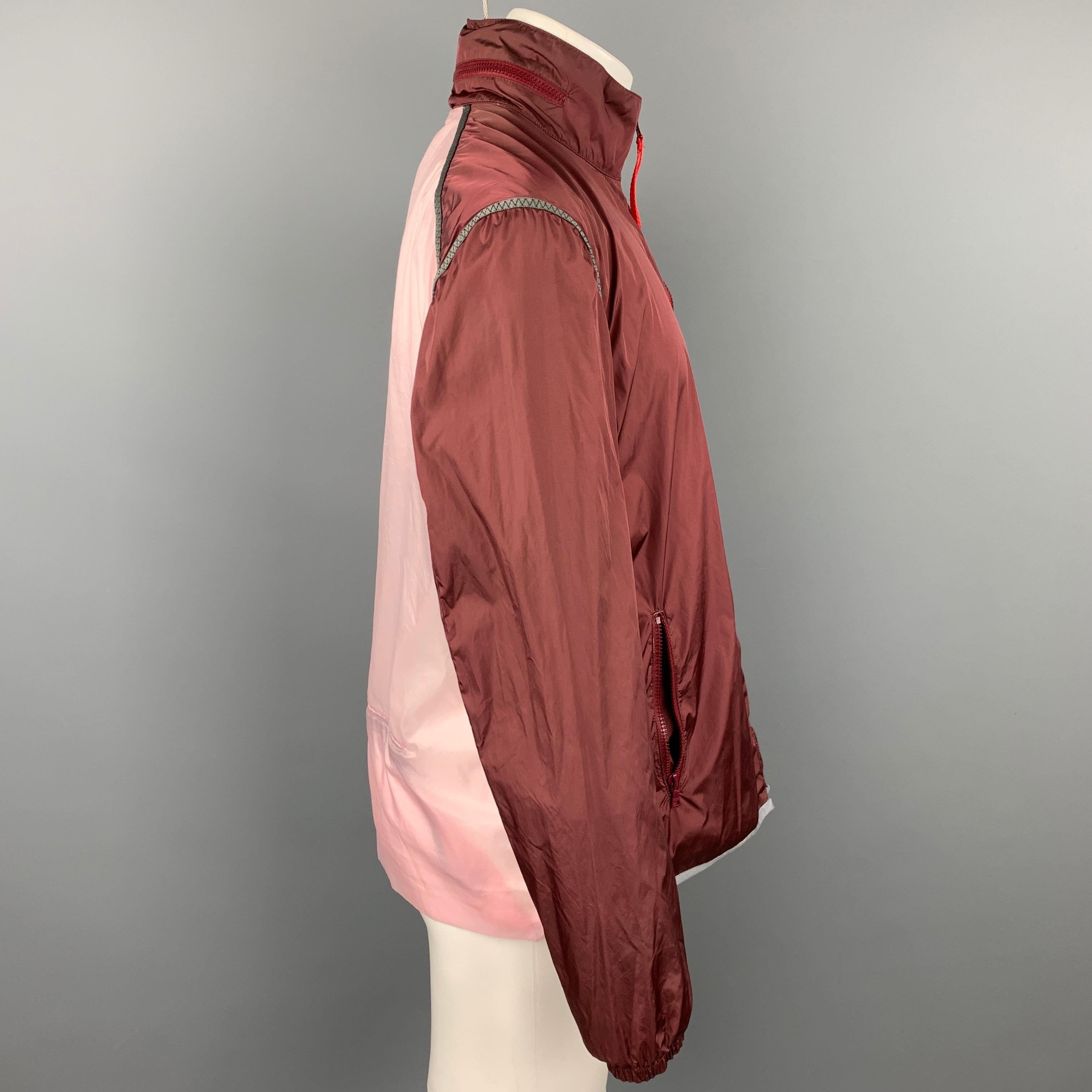 PRADA SPORT jacket comes in a burgundy & pink color block nylon featuring a hooded style, stripe trim, high collar, front pockets, and a full zip up closure. Made in Italy.

Very Good Pre-Owned Condition.
Marked: TG 50

Measurements:

Shoulder: 19