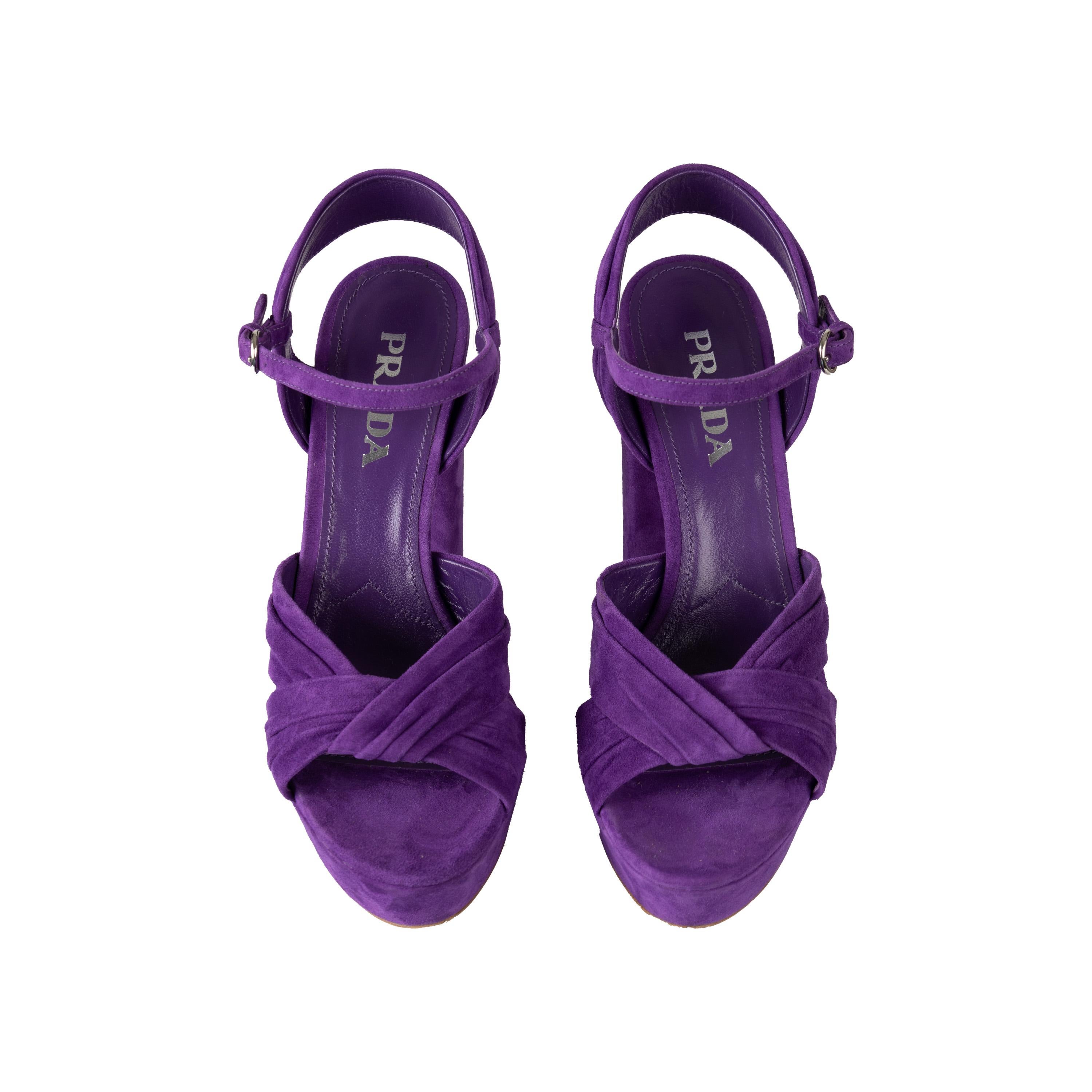 Ces talons compensés en daim de Prada offrent un look luxueux avec ses talons hauts peep toe et son style compensé. Confectionnées en daim souple de couleur violette, elles présentent une croix torsadée sur l'empeigne et une bride de cheville avec