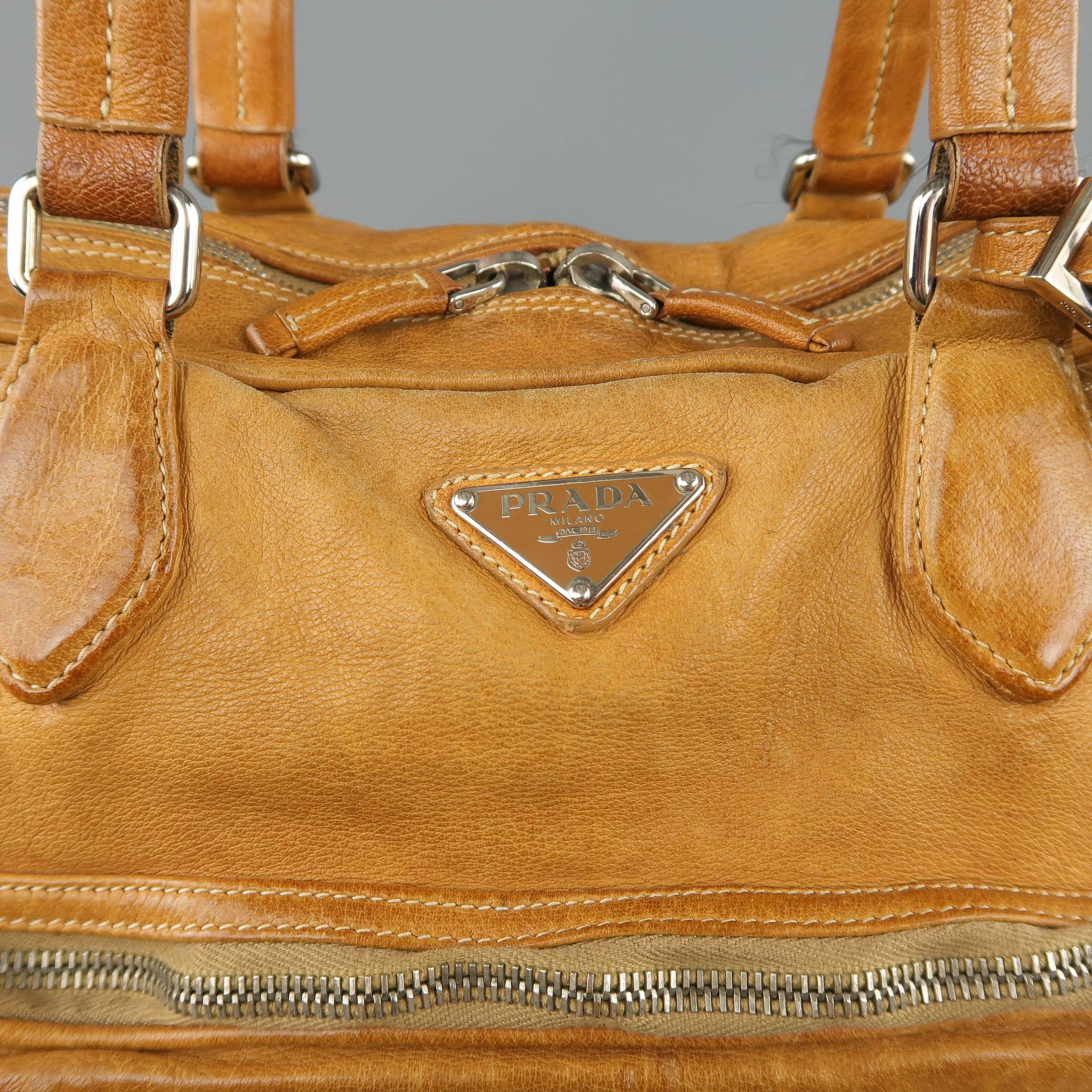 PRADA shoulder bag comes in aged tan leather with an enamel logo plaque, multiple zip patch pockets, double zip top closure, double top handles with luggage tag, and back pocket. Wear throughout leather. As-is. With dust bag. Made in Italy.
 
Fair