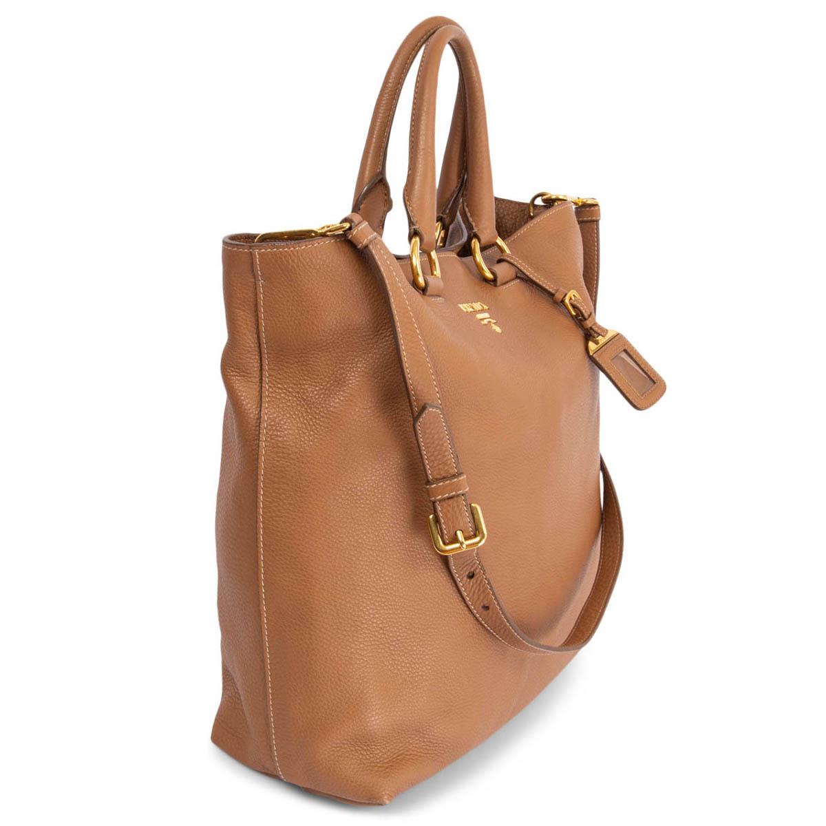 100% authentic Prada shopping tote bag in cognac grained leather featuring gold-tone hardware. Opens with a push-button on top and is lined dark brown logo nylon with one big zipper pocket against the back and a big open pocket against the front.