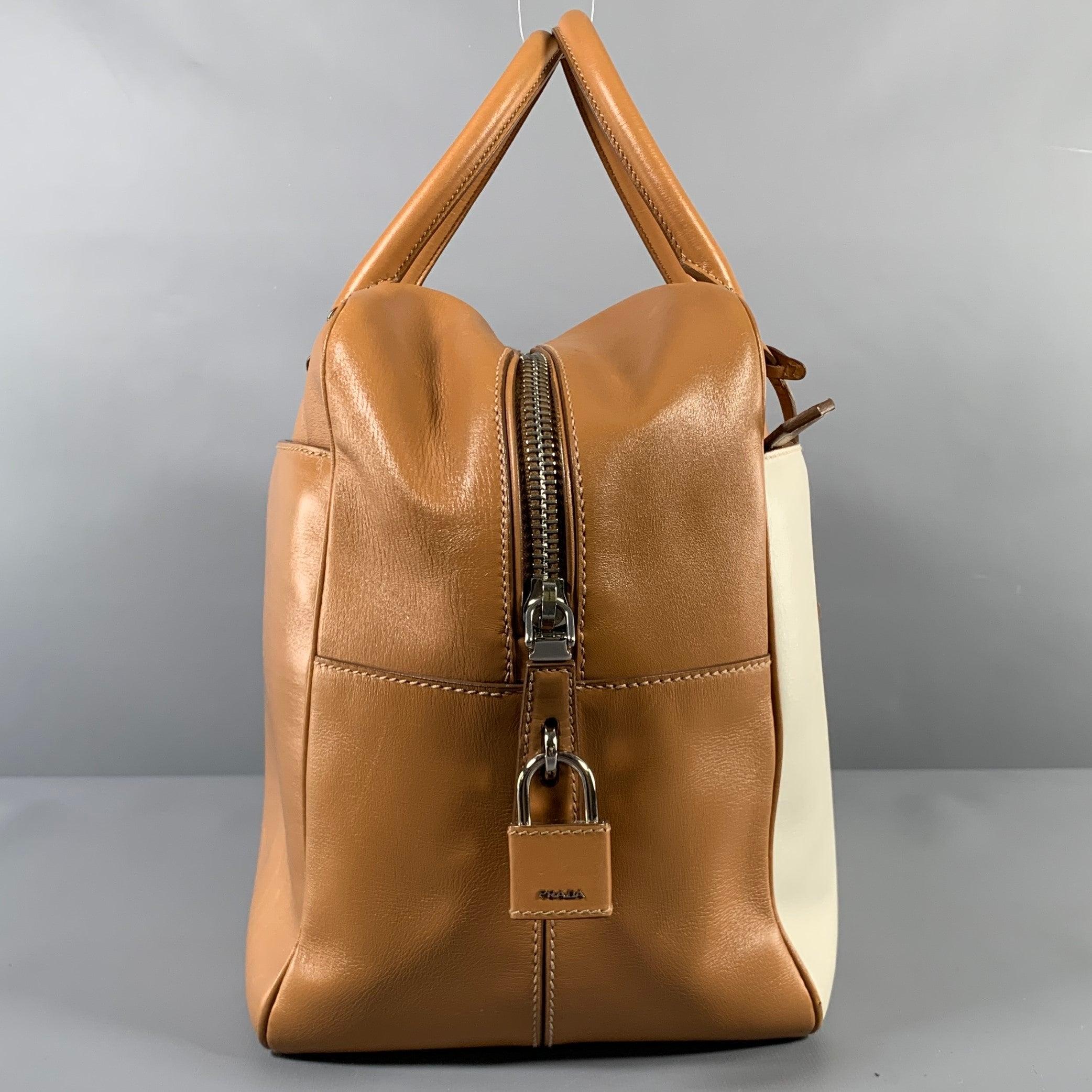 PRADA duffle bag comes in a tan and cream leather featuring a silver tone hardware, top handles, front zipper pocket, inner slots and pocket, name tag, lock & key and a top zipper closure. Includes dust bag. Made in Italy.Very Good Pre-Owned