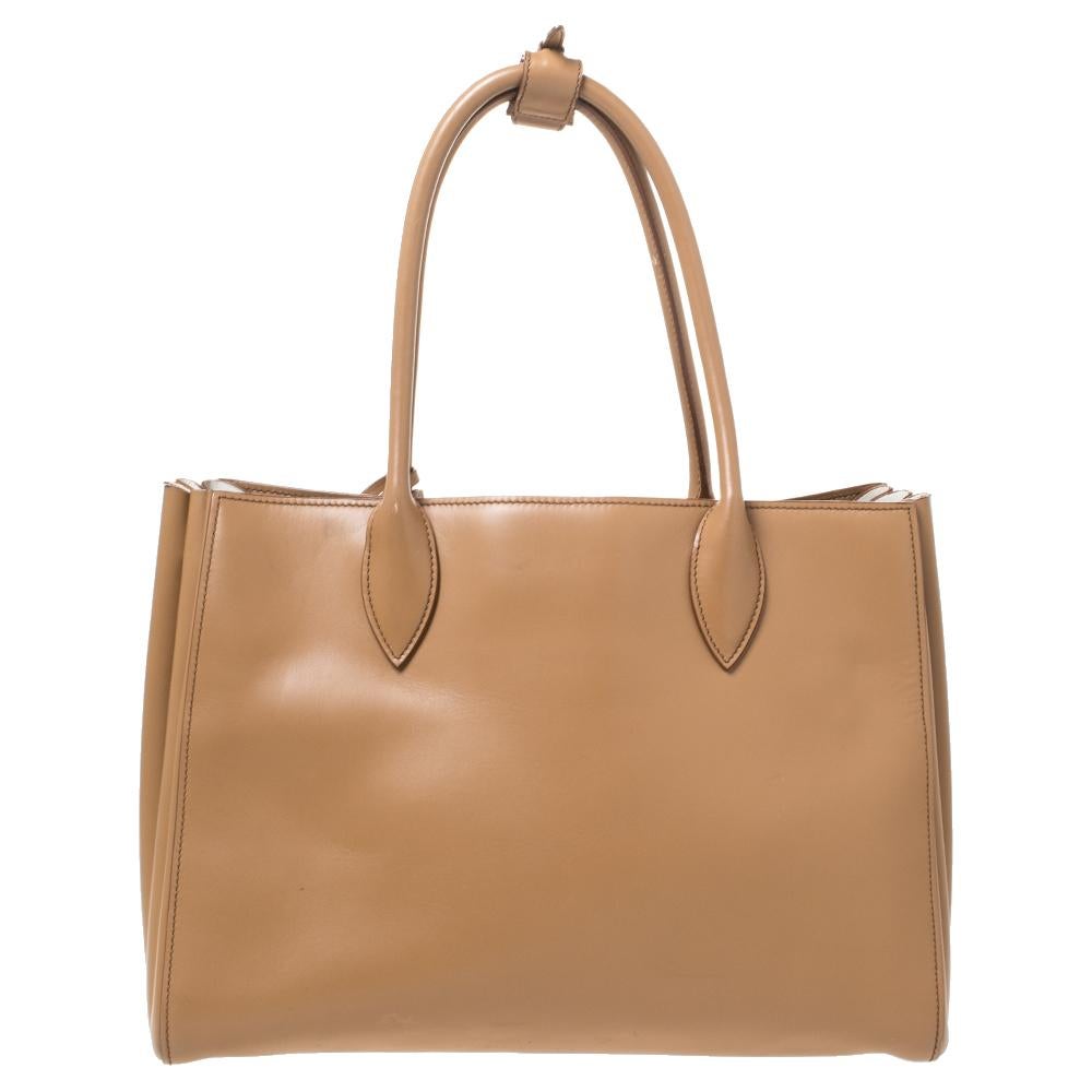 Feminine and stylish, this Bibliotheque tote from Prada is a worthy buy. Crafted from tan leather, the bag features dual top handles, a removable shoulder strap, the brand logo at the front in gold-tone and a leather tag. The nylon-lined interior is