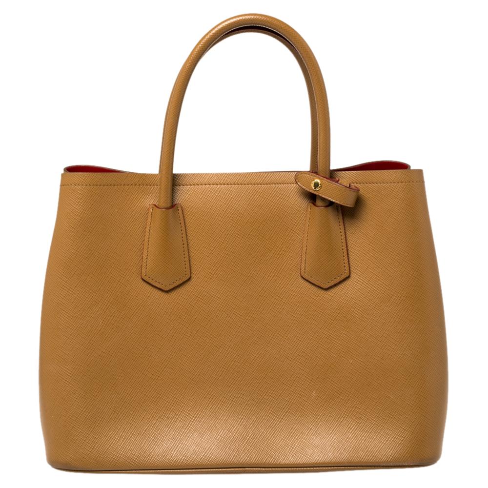 Flaunt your unique aesthetics in fashion with this fabulous tote from Prada. Simple and classy, it comes crafted from Saffiano Cuir leather in a tan shade and features dual top handles. It opens to a leather-lined spacious interior that can easily