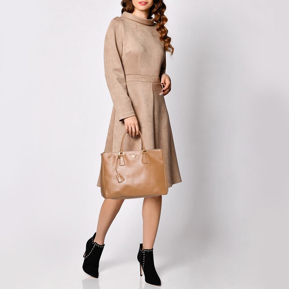 Loved for its classic appeal and functional design, Galleria is one of the most iconic and popular bags from the house of Prada. This beauty in tan is crafted from Saffiano Lux Leather and is equipped with two top handles, the brand logo at the