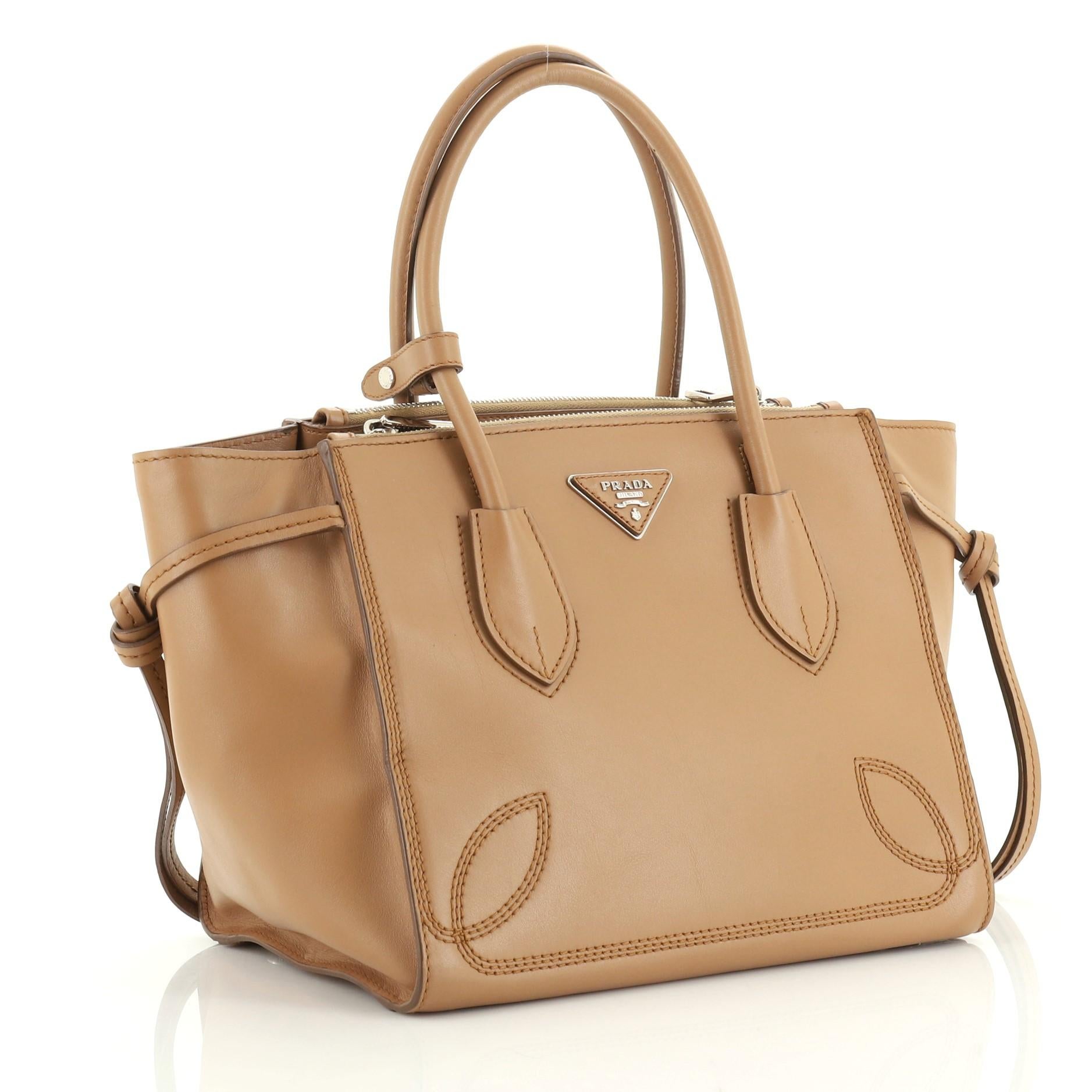 This Prada Tassel Twin Pocket Tote City Calf Small, crafted from brown calf leather, features dual rolled handles, leather tassels at the sides, and silver-tone hardware. It opens to a neutral fabric interior with zip closures and an open top middle