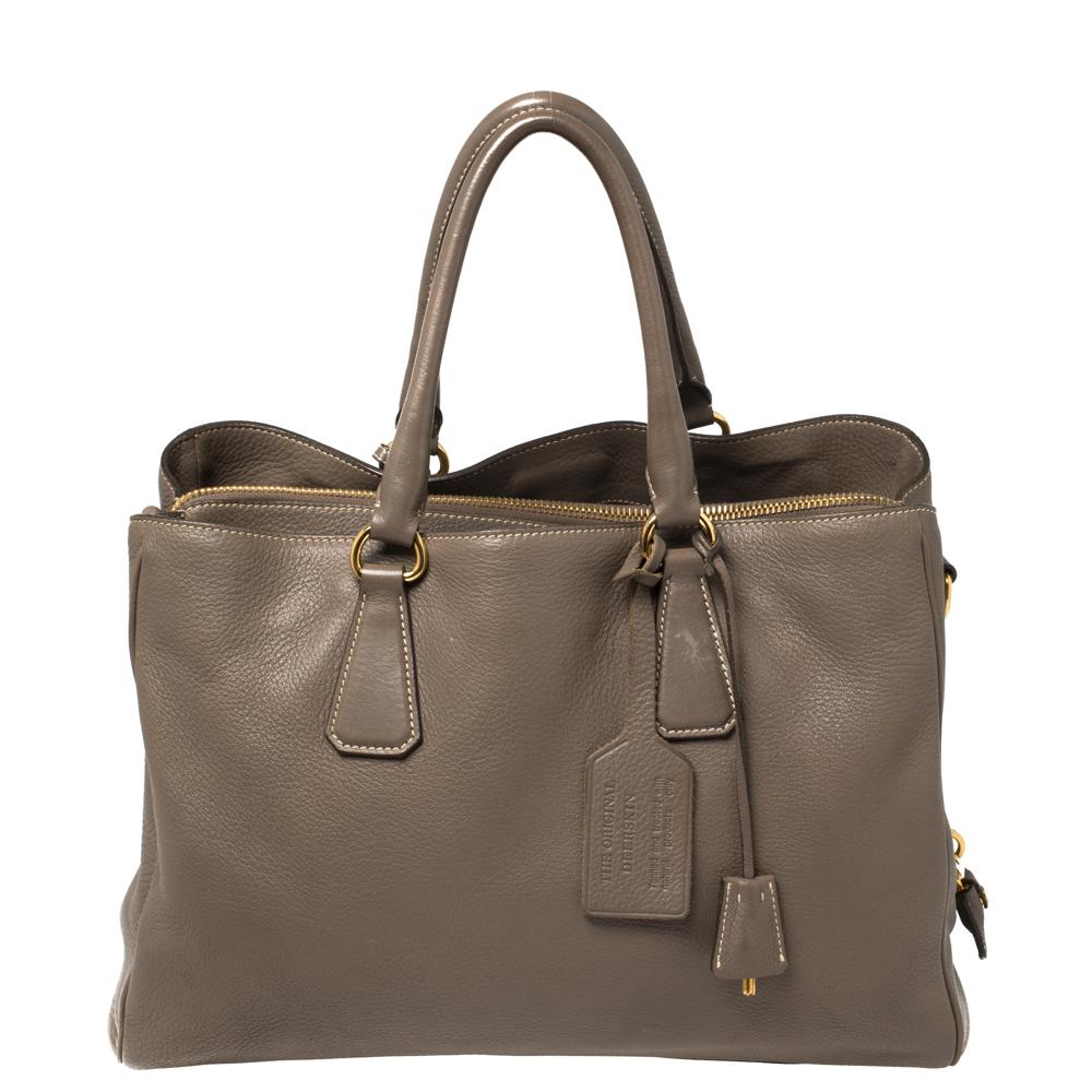 This elegant tote from Prada is crafted from leather and is perfect for daily use. The bag features double handles, protective metal feet, side zippers, and gold-tone hardware. The nylon-lined interior is spacious enough to hold all your