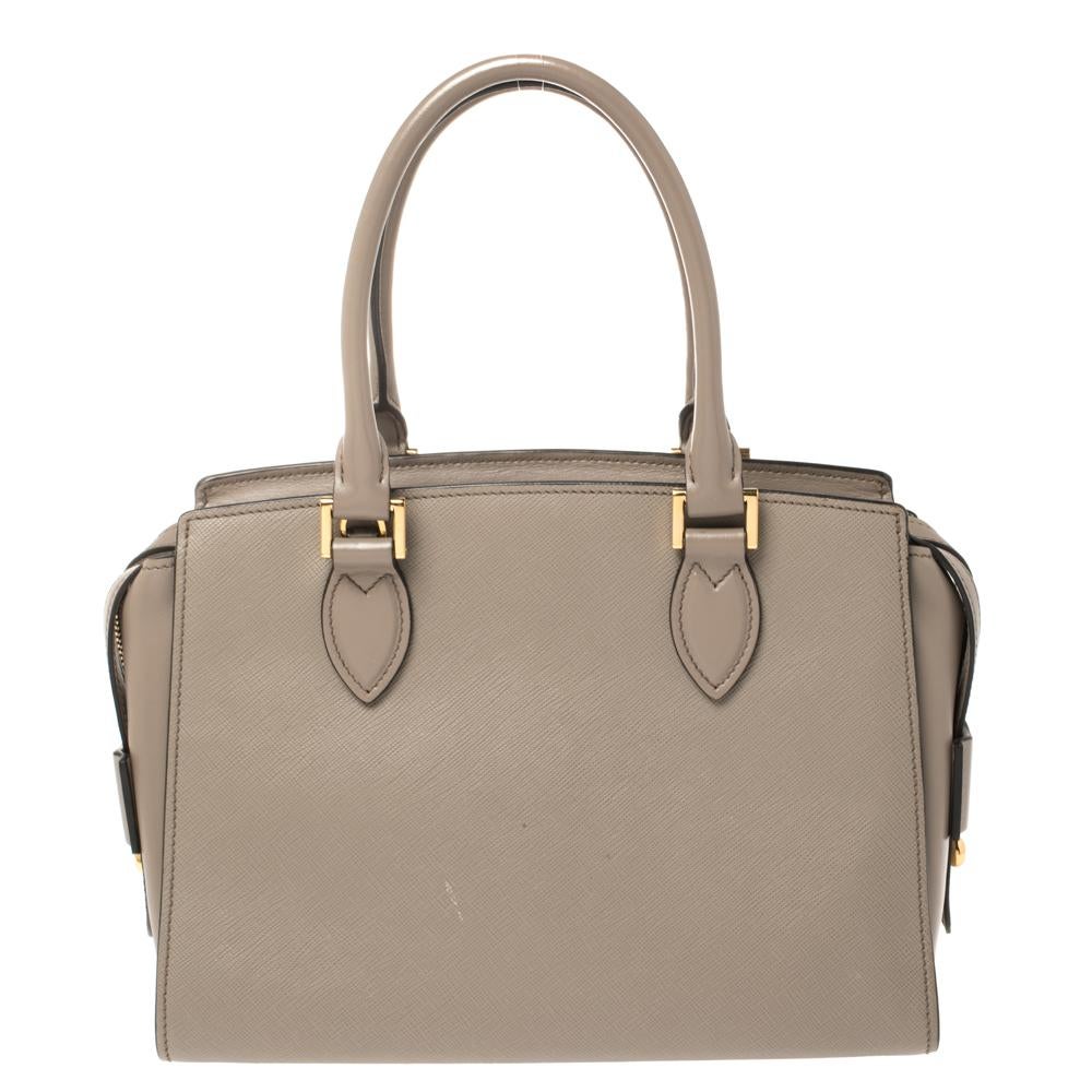 Este bolso Prada Borsa A Mano tiene una forma tan bonita que seguro que irás a la moda siempre que lo lleves. Está fabricada en piel saffiano gris y diseñada con dos asas y una cremallera que conduce a un interior de nailon. Este bolso, con un