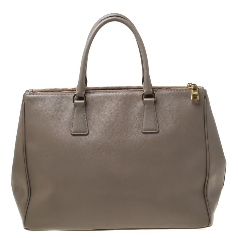 Feminine in shape and grand on design, this Double Zip tote by Prada will be a loved addition to your closet. It has been crafted from leather and styled minimally with gold-tone hardware. It comes with two top handles, two zip compartments and a