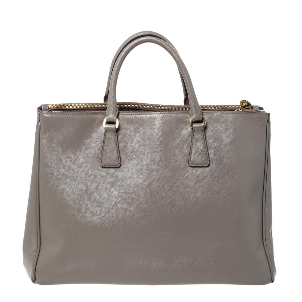 Feminine in shape and grand on design, this Double Zip tote by Prada will be a loved addition to your closet. It has been crafted from Saffiano Lux leather and styled minimally with gold-tone hardware. It comes with two top handles, two zip