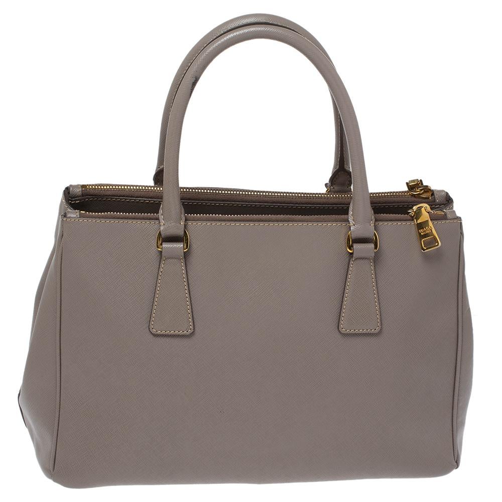 Luxury and class are displayed in this bag from Prada. It is made of the signature Saffiano leather in the taupe shade. This is a bag that comes with two handles, a detachable strap and the brand's logo fitted on the front in gold-tone. This Double