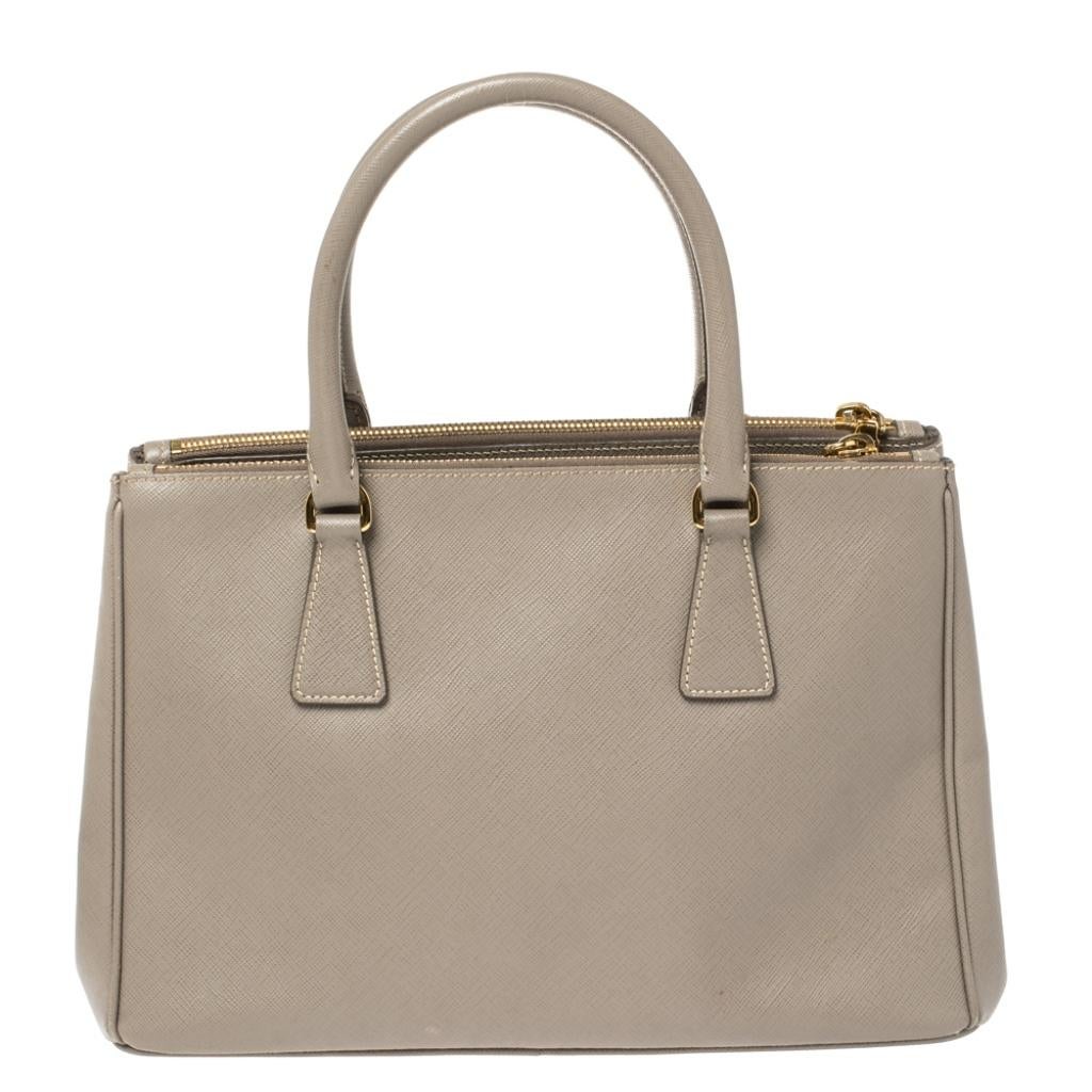 High on style and class, this Galleria Double Zip tote by Prada will be a cherished addition to your closet. It has been crafted from Saffiano Lux leather in a taupe shade and styled minimally with gold-tone hardware. It comes with dual handles and
